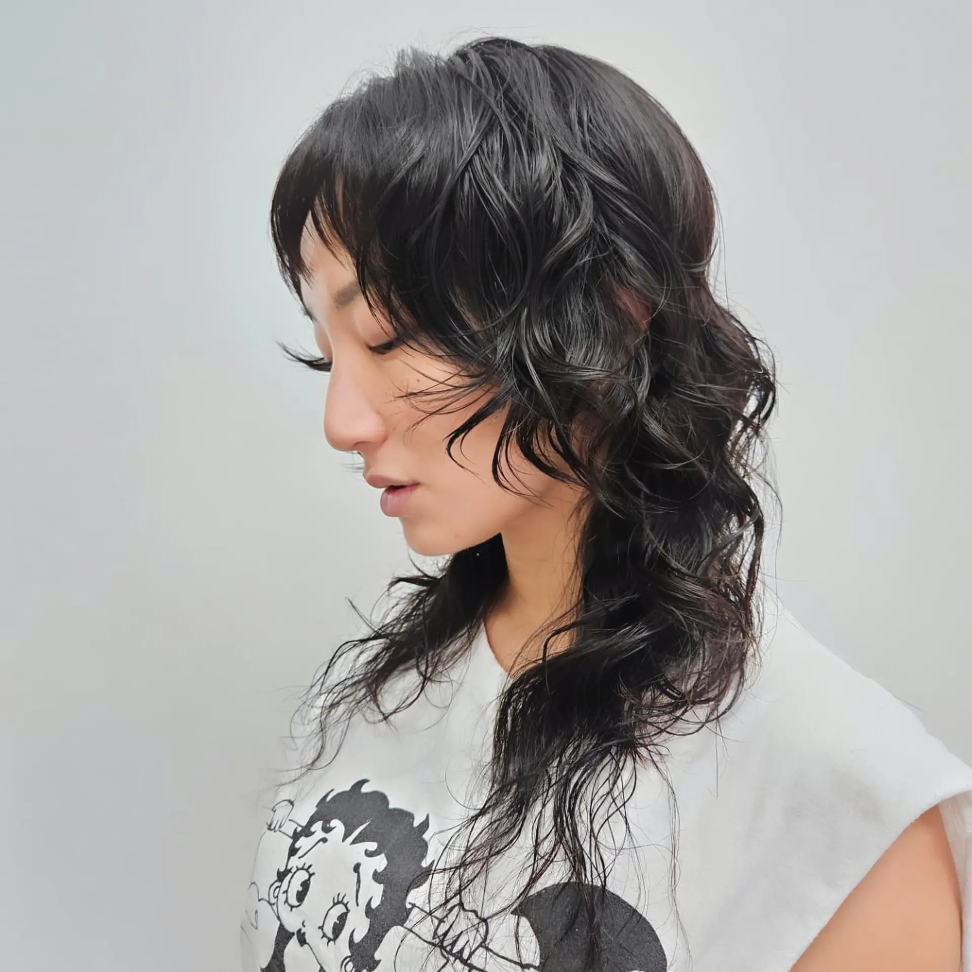 A textured black shaggy mullet featuring wispy micro bangs, voluminous layered crown, and soft wavy strands falling past the shoulders. 1