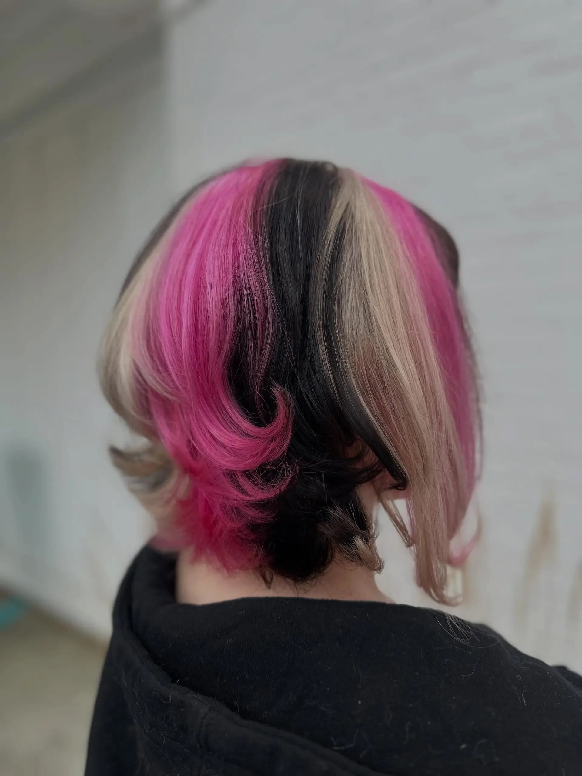 A short layered bob styled with distinct color-blocked sections in hot pink, cool blonde, and deep black. 1
