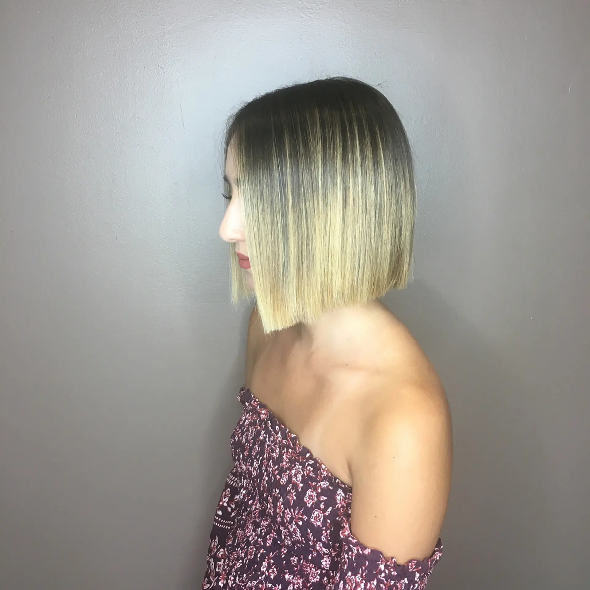 A sleek, chin-length blunt bob featuring fine blonde highlights seamlessly blended with a dark root shadow. 1