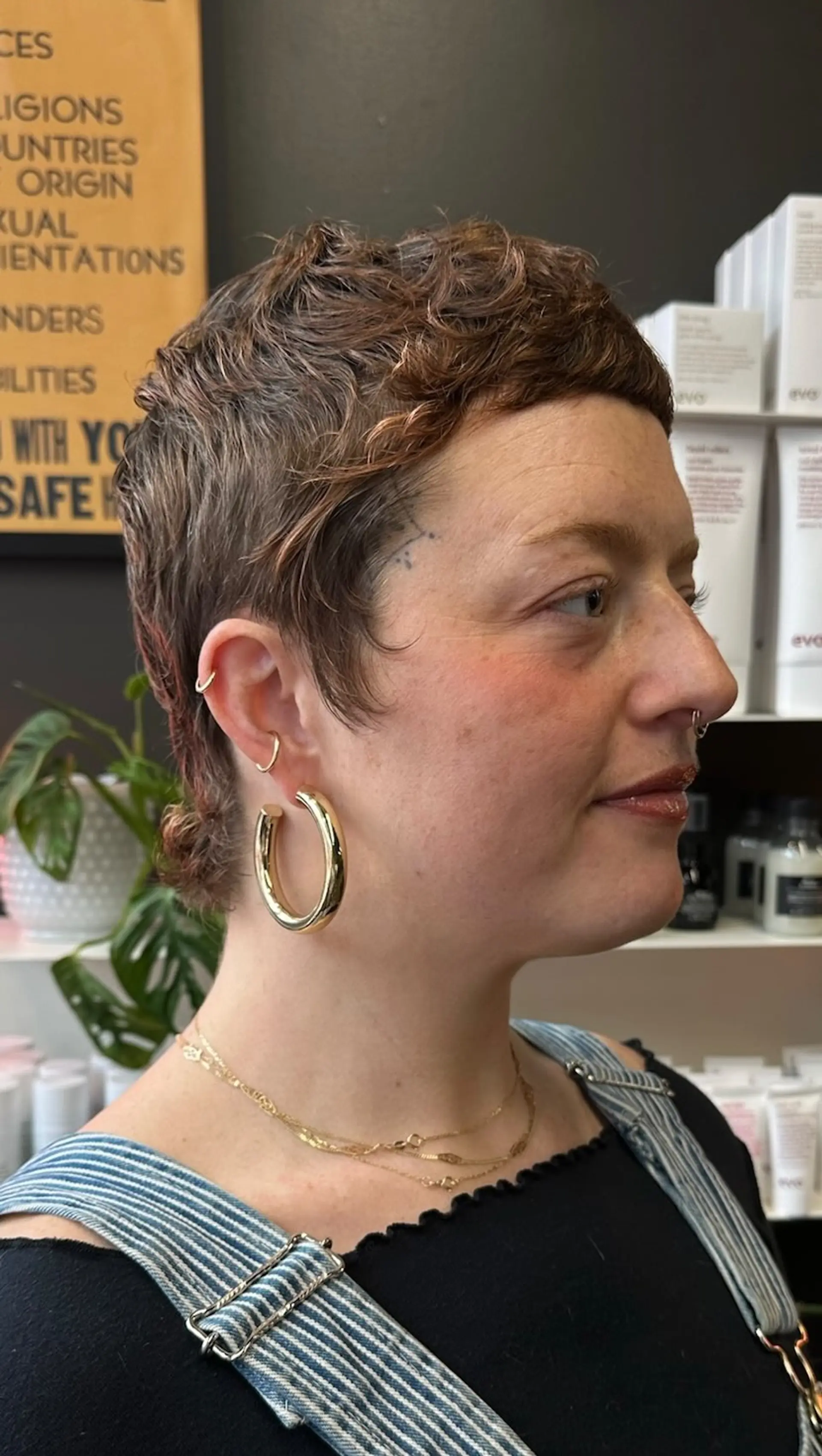 A textured brunette mixie haircut featuring micro bangs and soft flicked layers at the nape. 1