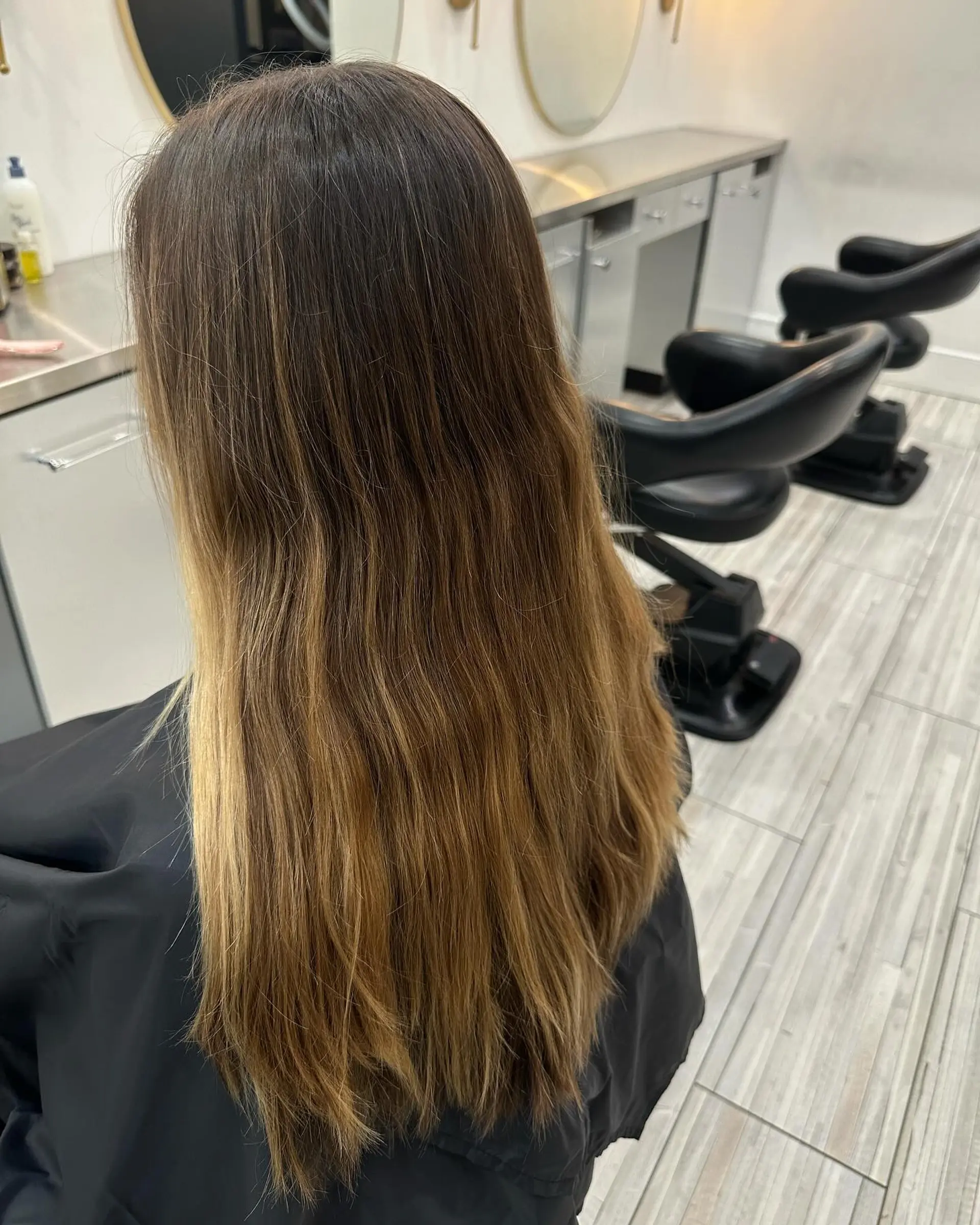 Long dark brunette hair featuring a seamless transition into warm caramel and golden blonde balayage tones. 1