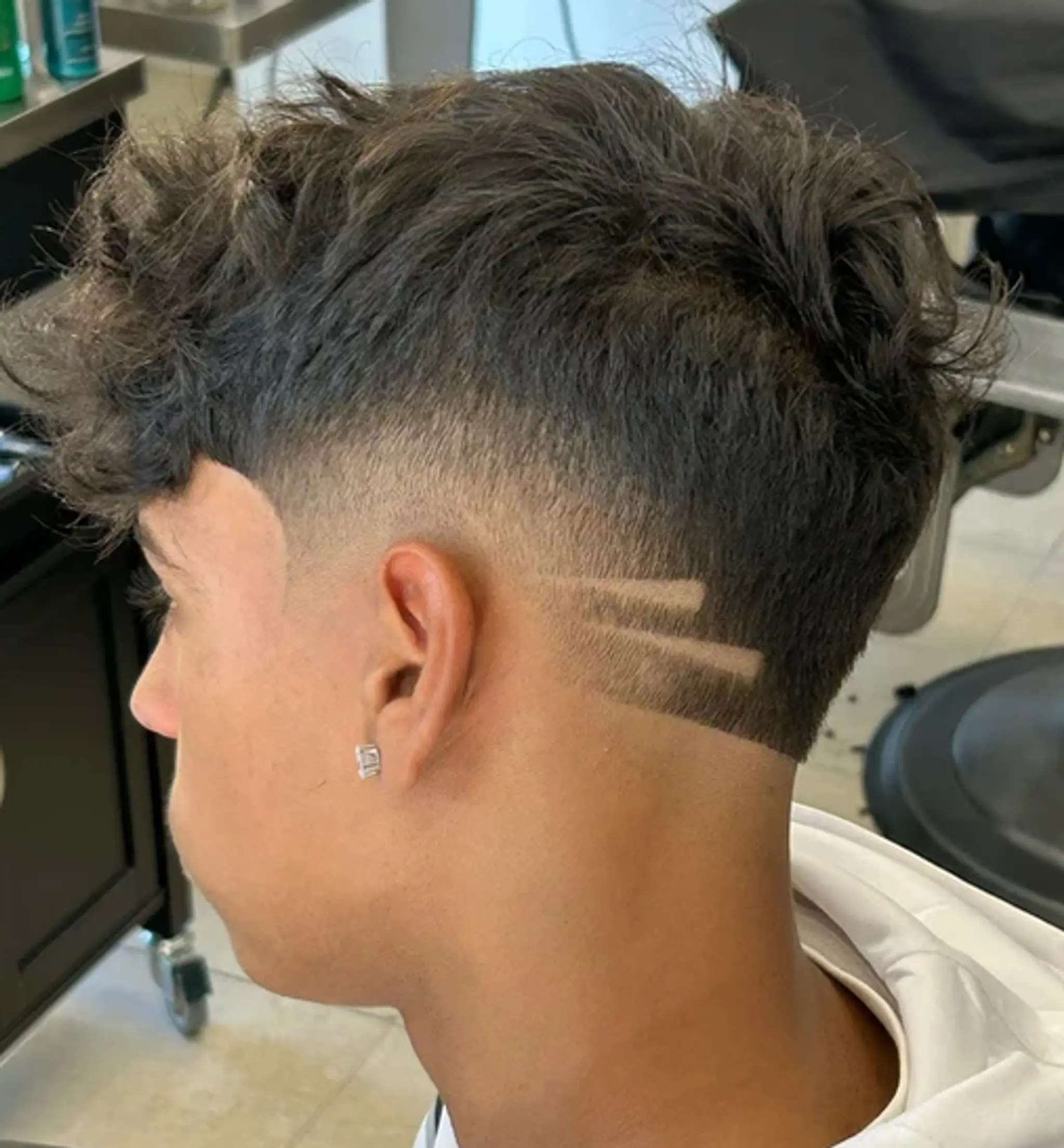 A short, curly hairstyle with a low fade and geometric razor lines.