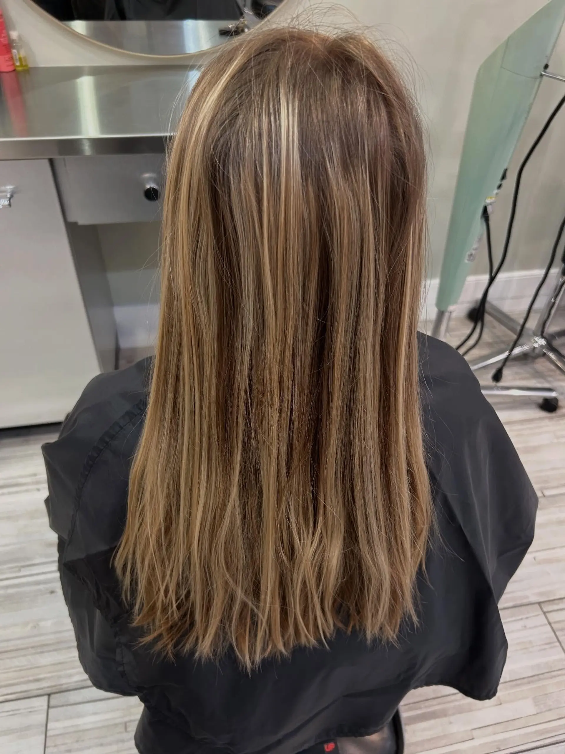 Straight, mid-back length hair styled smoothly with dense, dimensional warm blonde partial highlights. 1