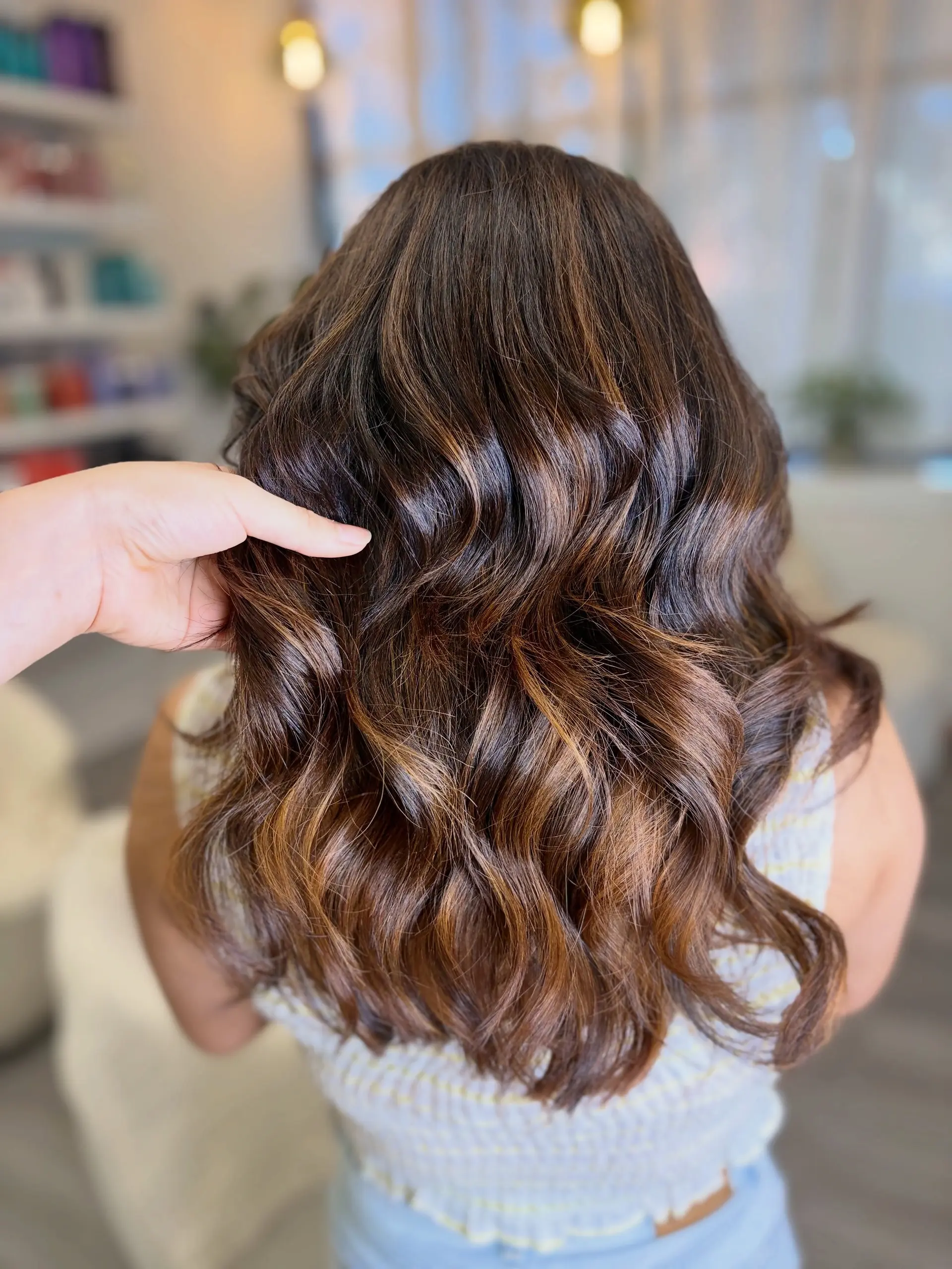 Medium-length dark brunette hair featuring warm caramel balayage styled in loose, polished waves. 1
