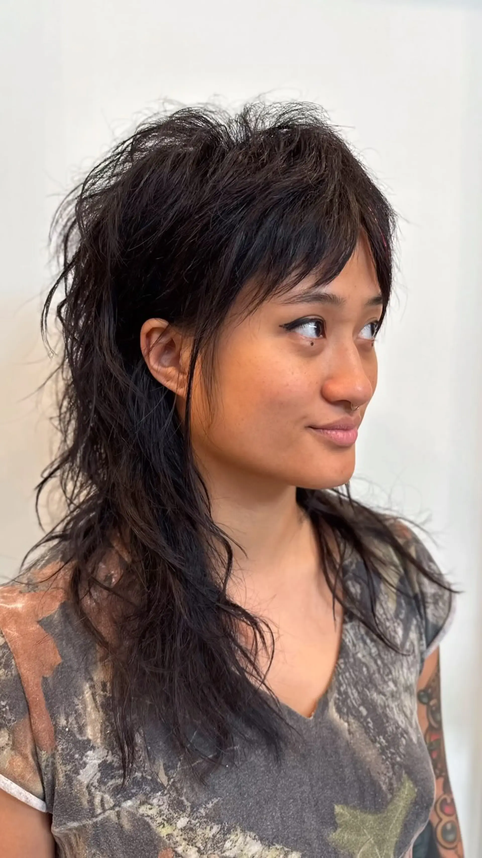 A textured modern wolf cut mullet featuring choppy piecey bangs, voluminous layered crown, and tapered ends. 1