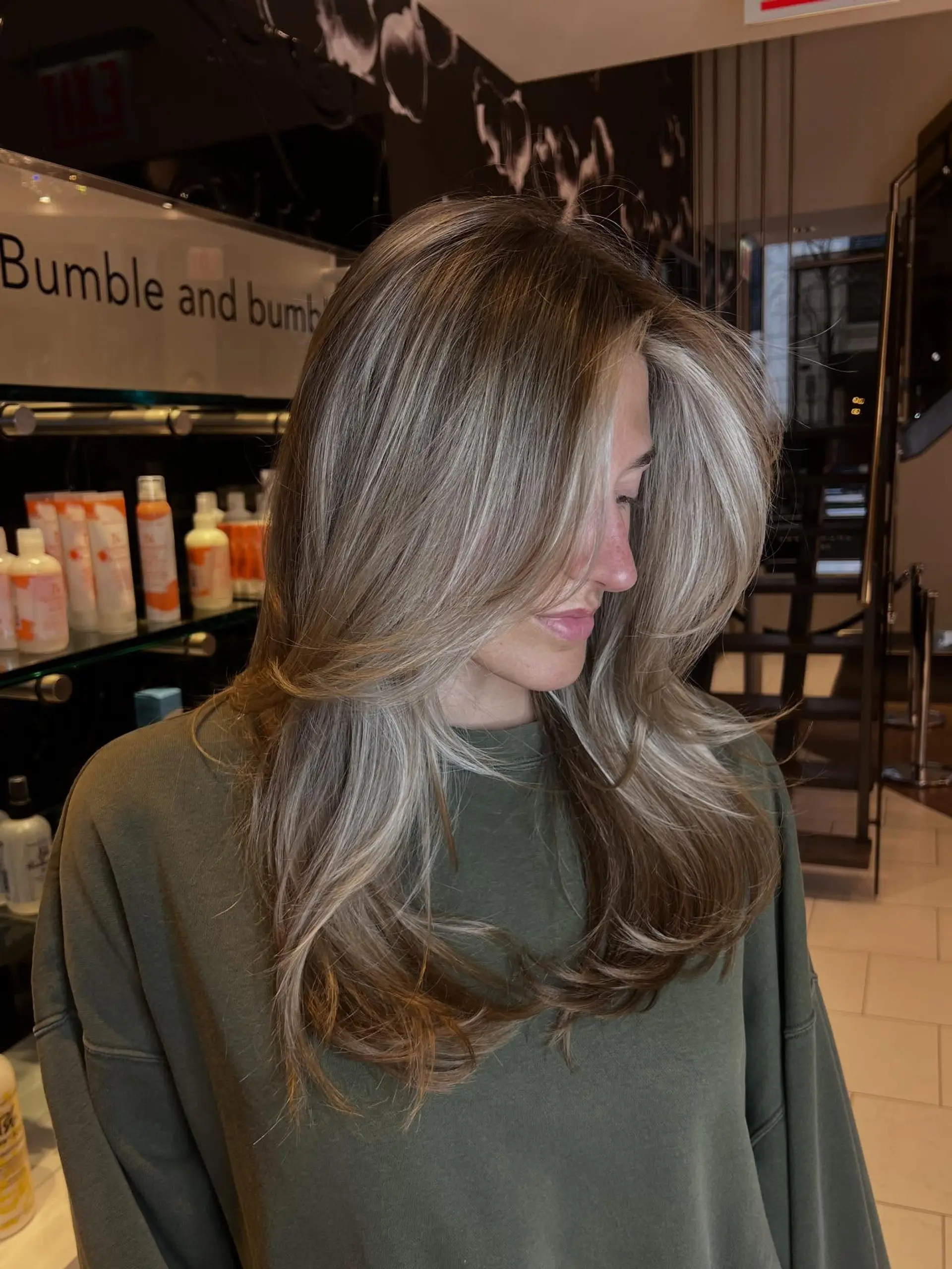 Long layered cut styled into a bouncy blowout with sweeping face-framing curtain layers, dimensional blonde foil highlights, and a bright money piece. 1
