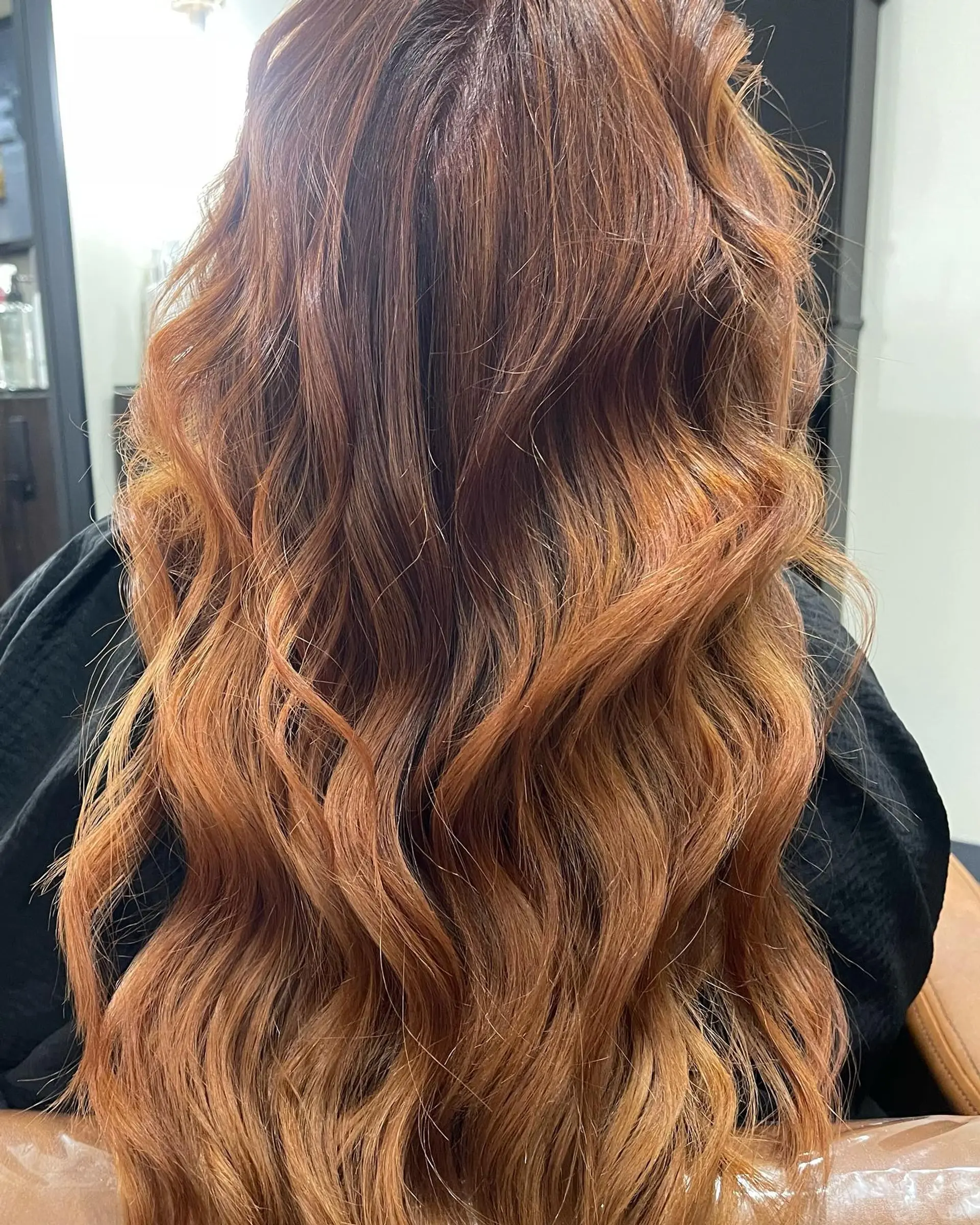 Long warm copper hair styled into loose, textured waves cascading down the back. 1