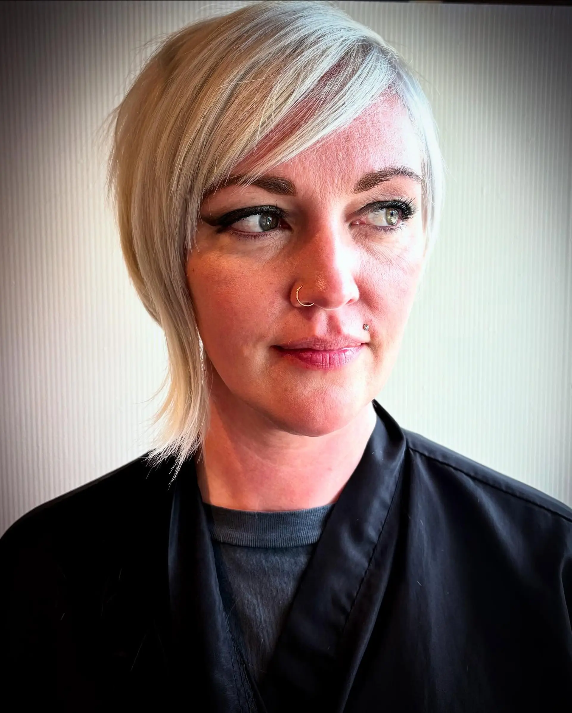 A modern asymmetrical pixie cut styled with deep side-swept bangs in an icy platinum blonde tone. 1