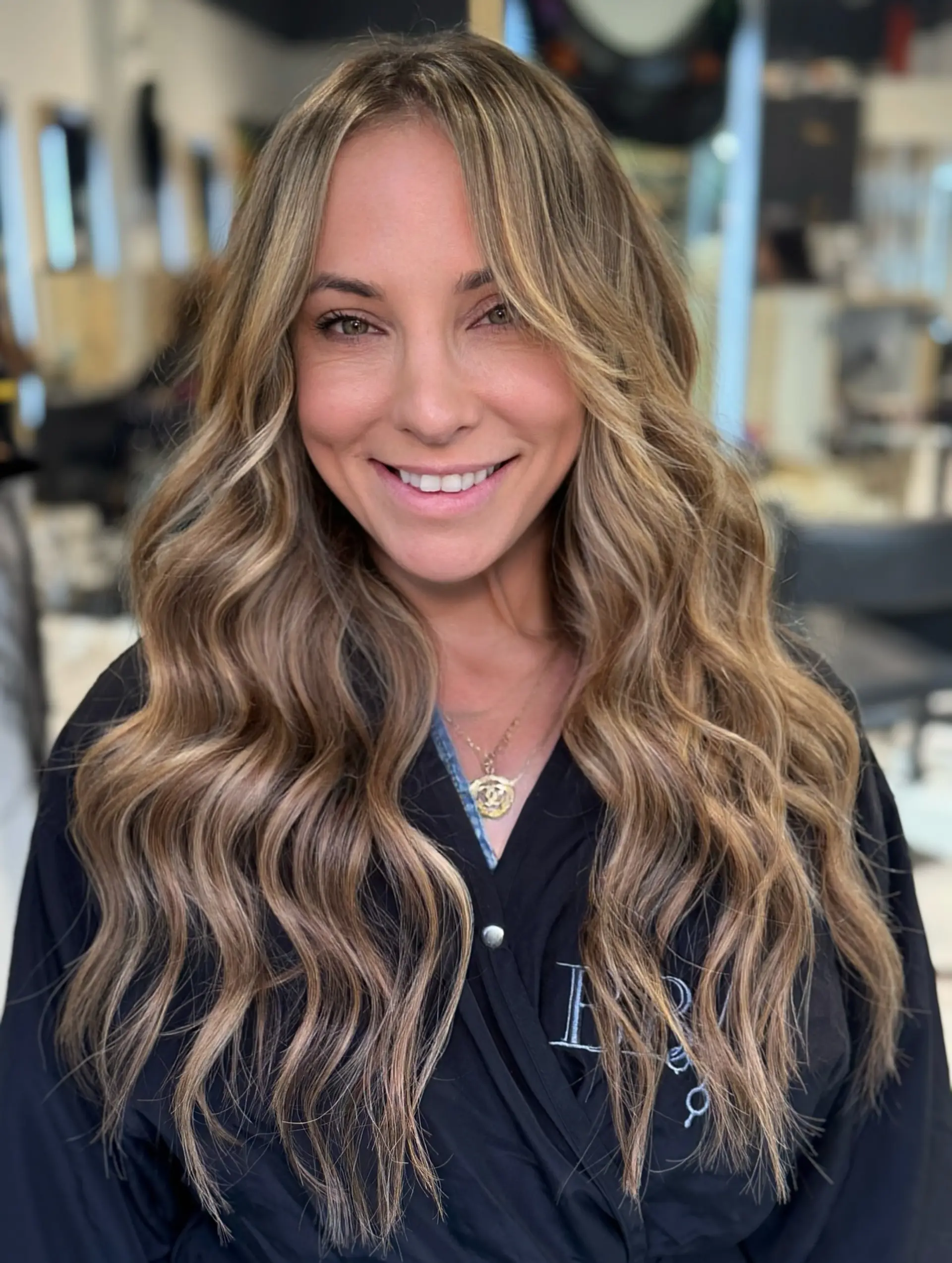 Long bronde hair styled with voluminous beach waves, curtain-style framing, and seamlessly blended tape-in extensions. 1