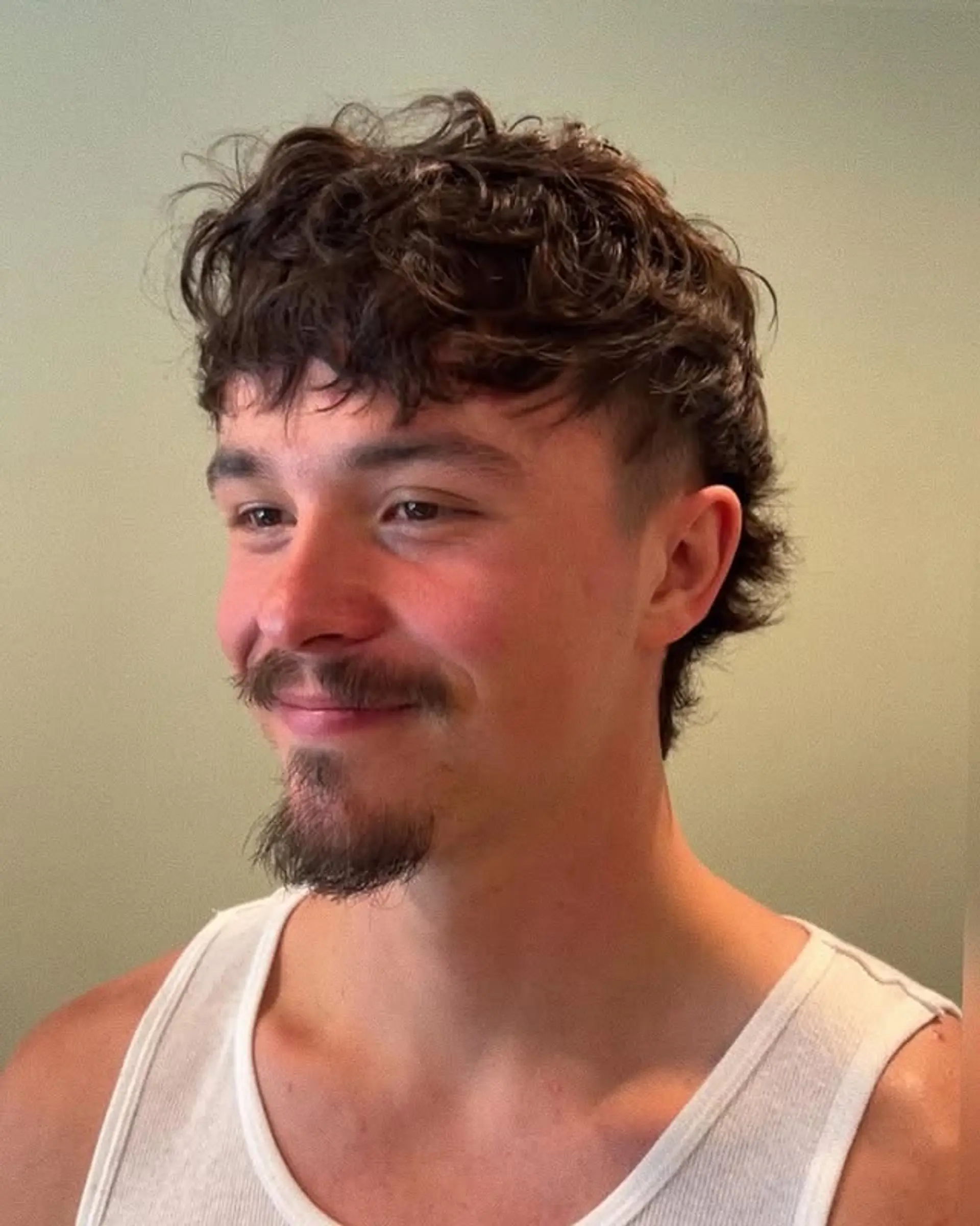 A stylish, curly mullet with a textured top and a contemporary taper fade on the sides. 1