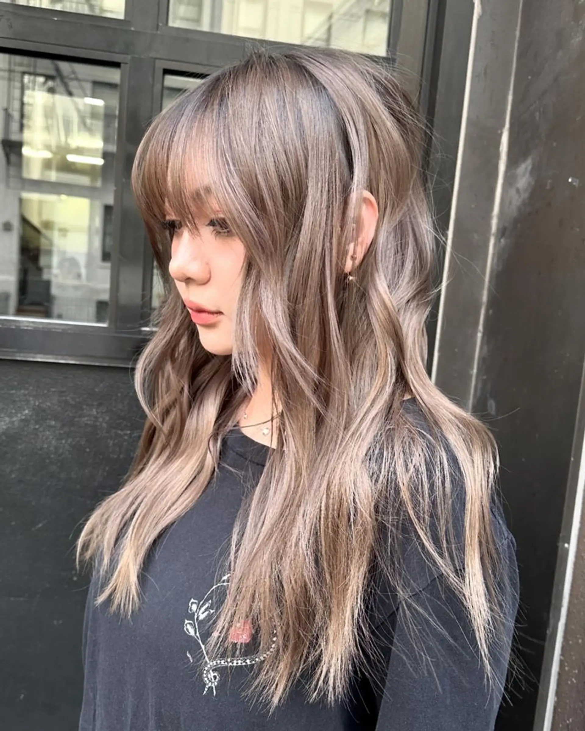 Long, wavy hair with ash blonde and cool brown dimensional color, featuring layered cuts and side-swept bangs for added movement and a soft, flattering focus. 1