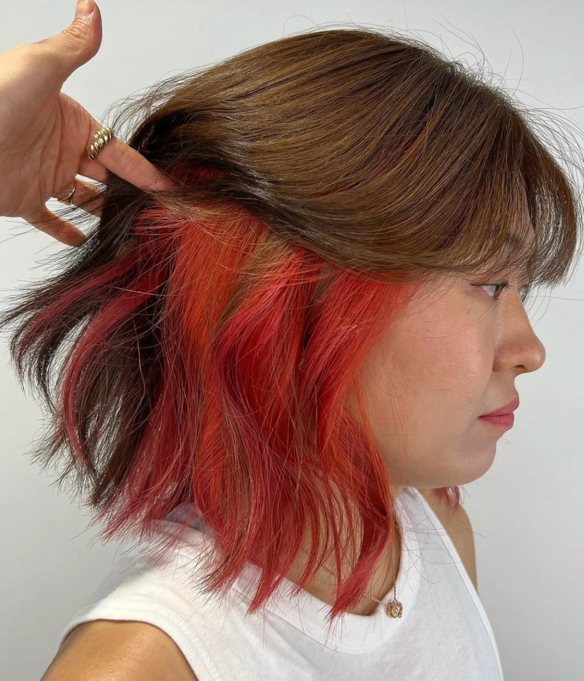 Shoulder-length, medium bob with wavy texture and a two-tone color scheme: warm brown on top and red underlayer. Includes side-swept bangs.