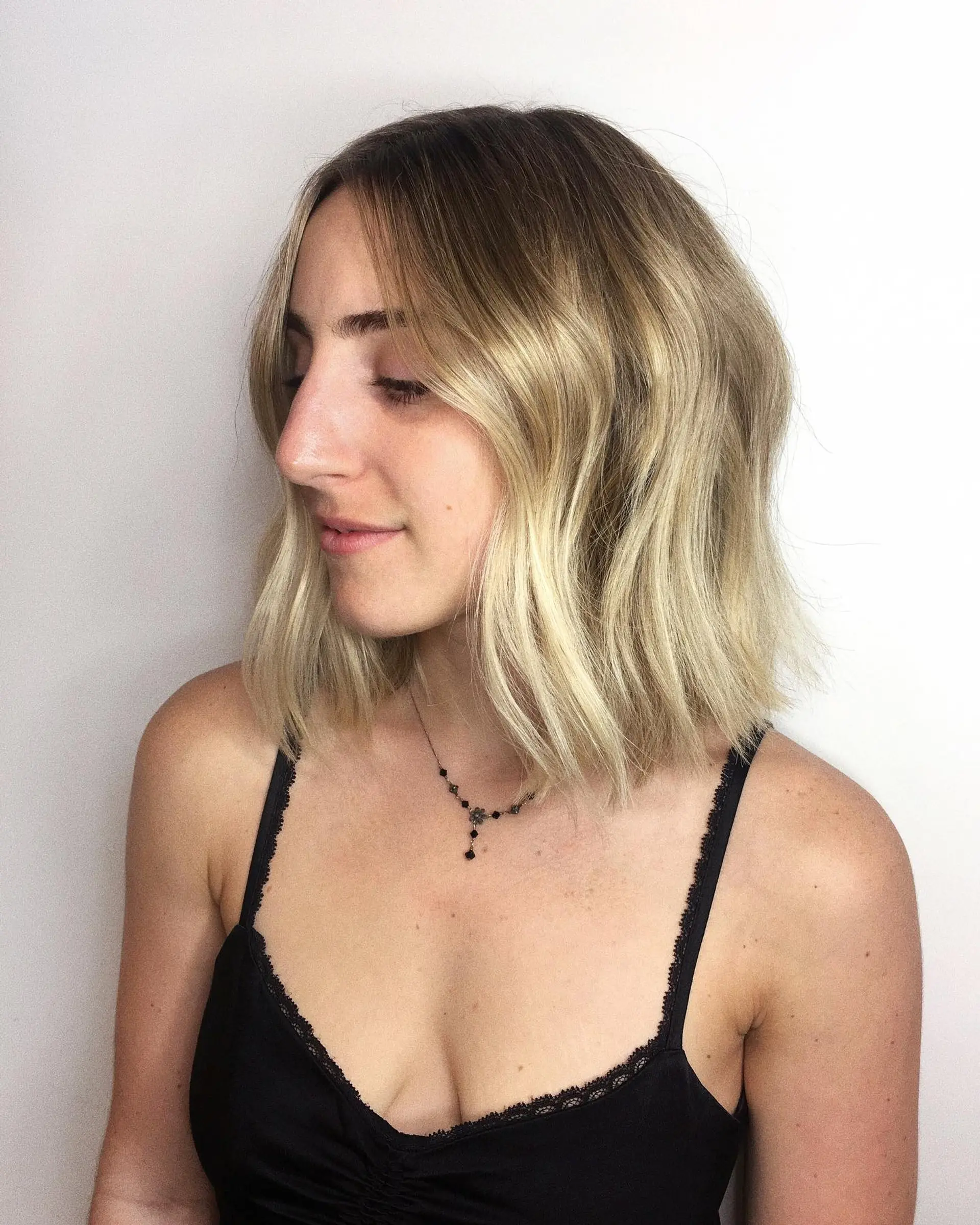 A shoulder-length wavy lob with root melt and bright blonde balayage highlights. 1