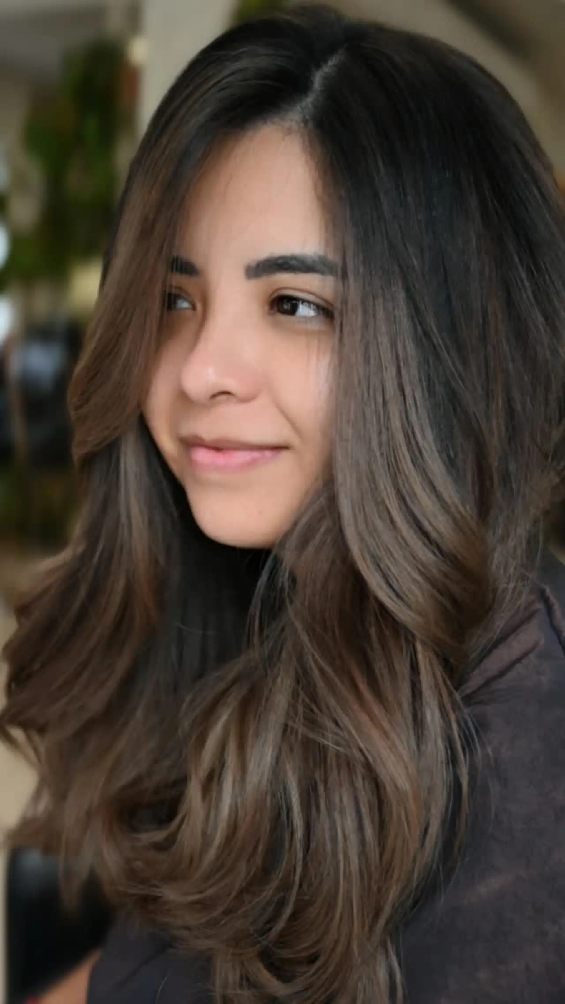 Long dark brown hair styled in soft, bouncy waves with face-framing layers and subtle ash brown highlights. 1
