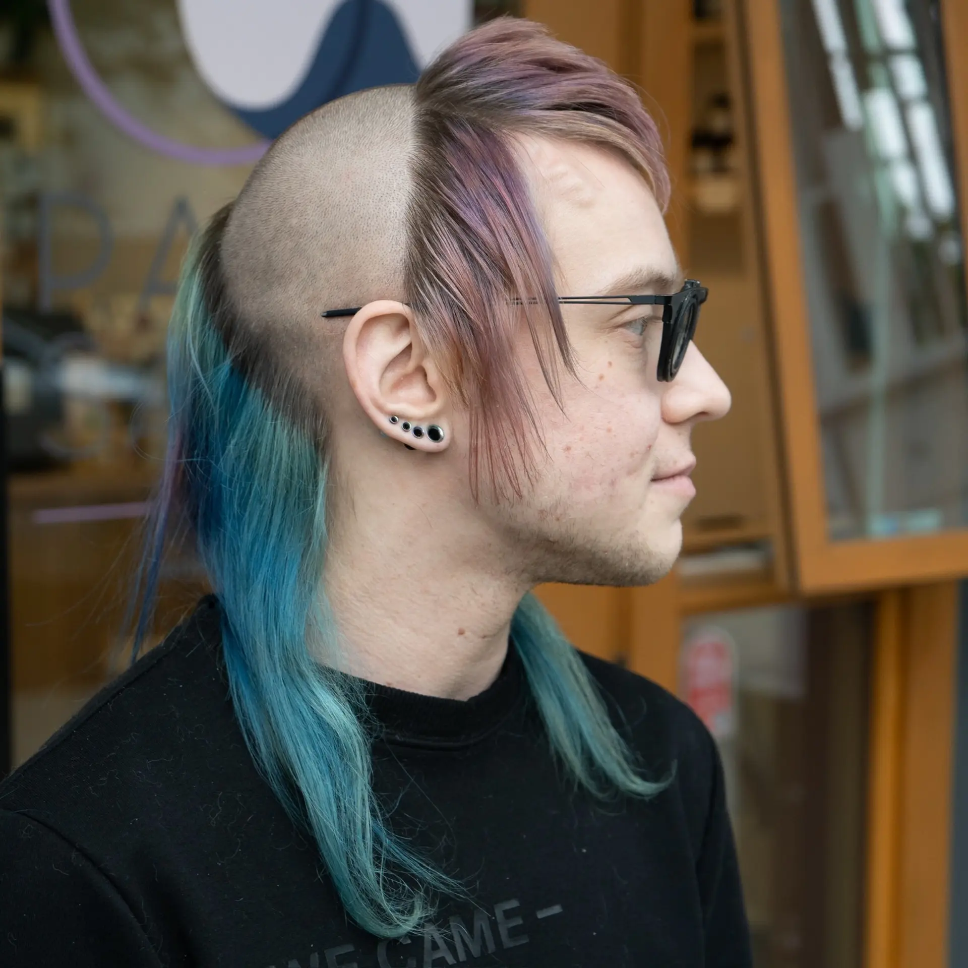 An avant-garde, extreme mullet featuring completely shaved sides and crown, contrasted with textured pastel fringe in the front and long, vibrant teal lengths flowing down the nape. 1