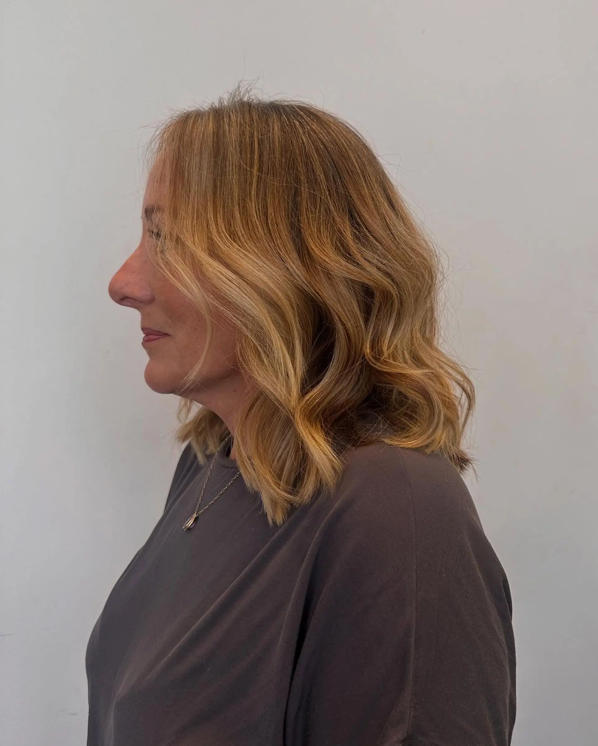A shoulder-grazing one-length haircut styled into soft, beachy waves with warm golden blonde highlights. 1