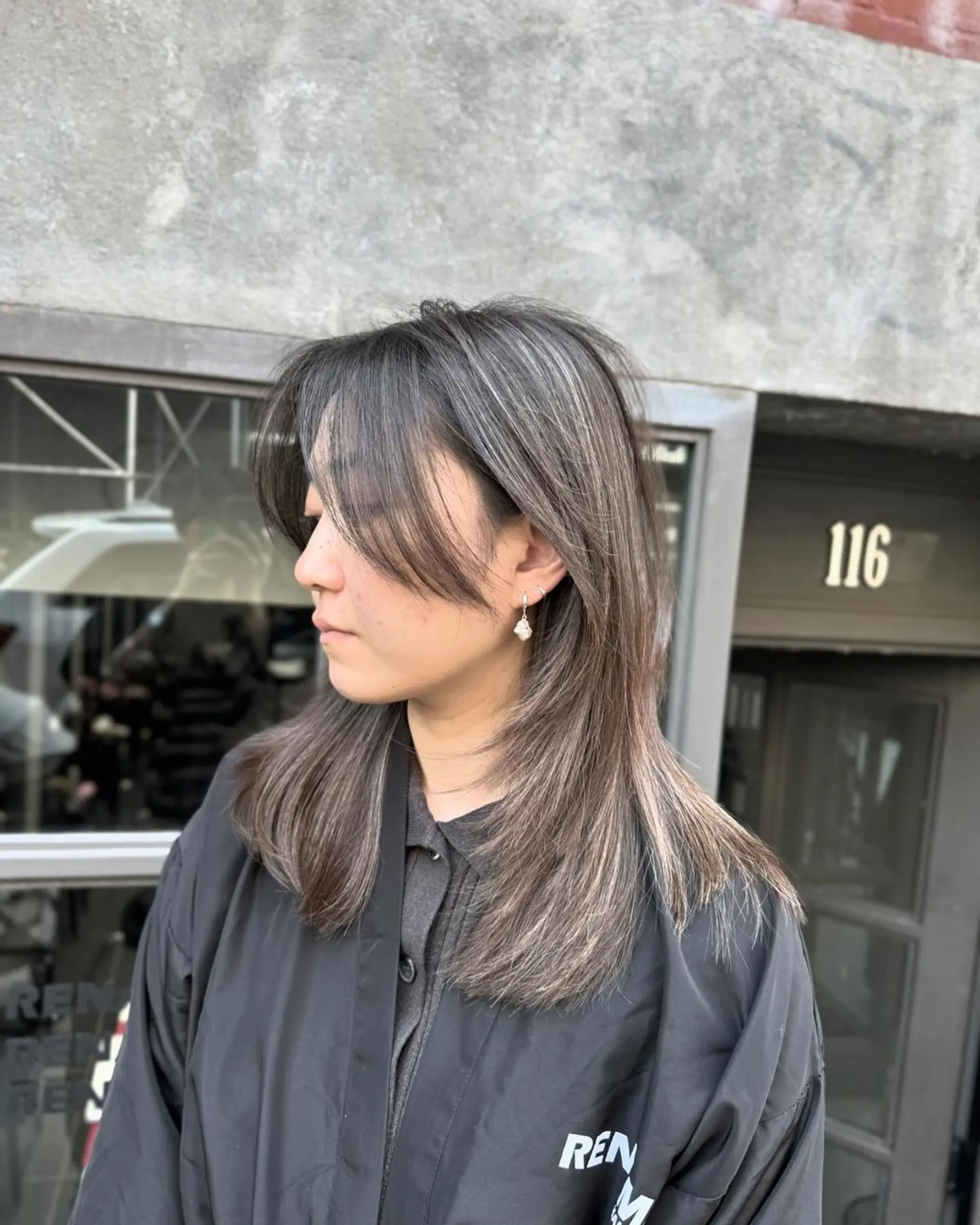 A contemporary hairstyle featuring straight, layered tresses of medium length with a dark brown base color and subtle silver highlights. Feathered layers and soft side bangs frame the face. 2