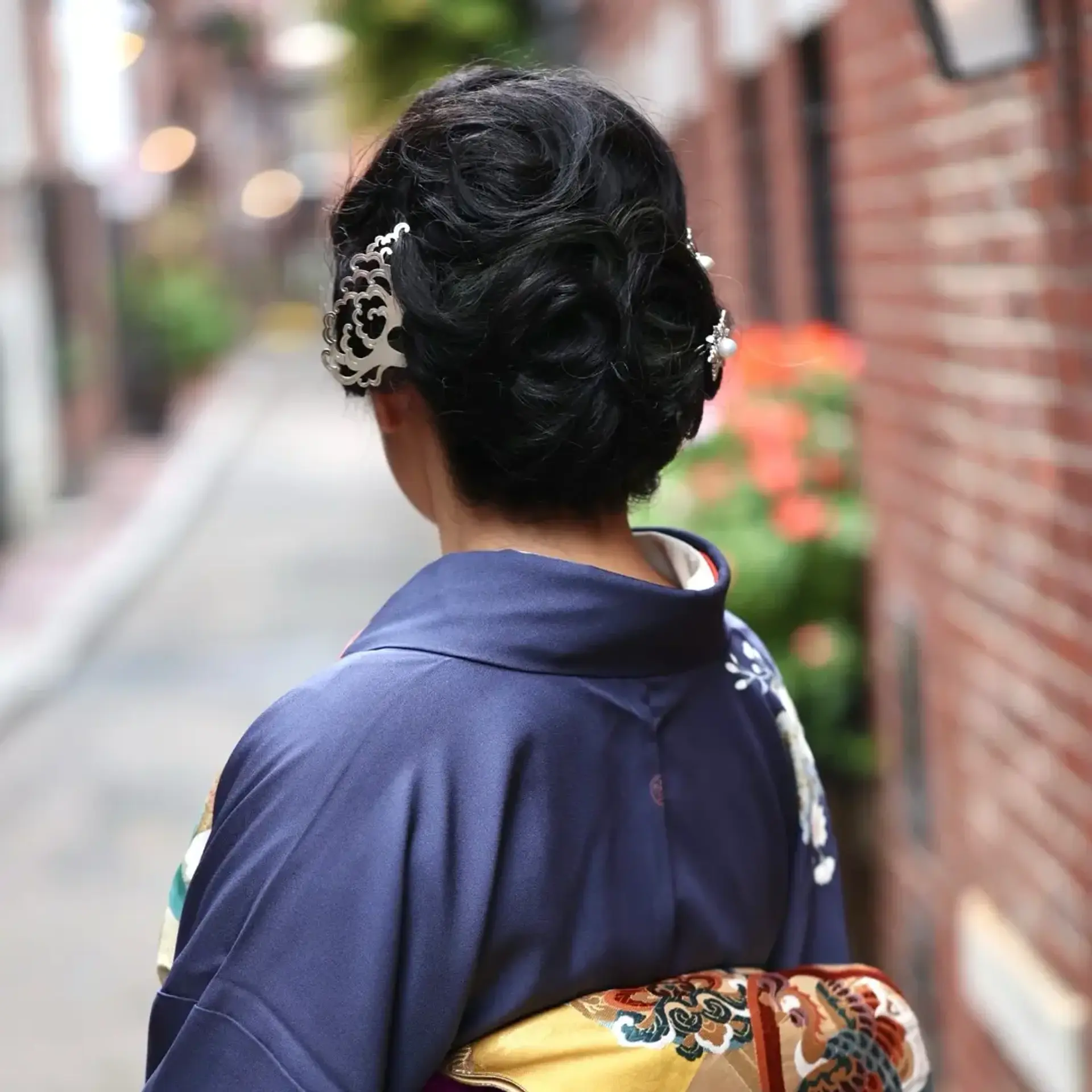 An elegant formal updo styled with textured rolls and pin curls, accessorized with decorative hairpins to complement traditional kimono attire. 1