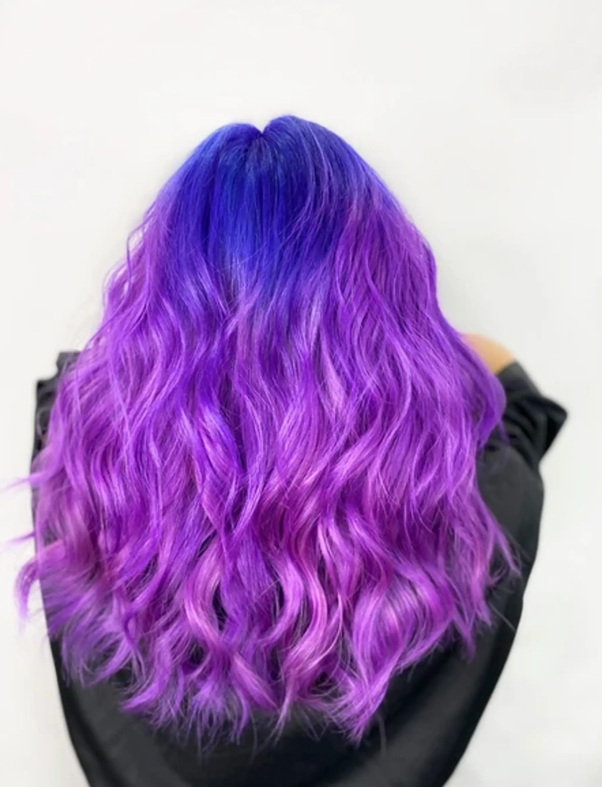 Medium-length hair with a striking gradient from deep blue at the roots to vibrant purple at the ends, styled in lively waves.