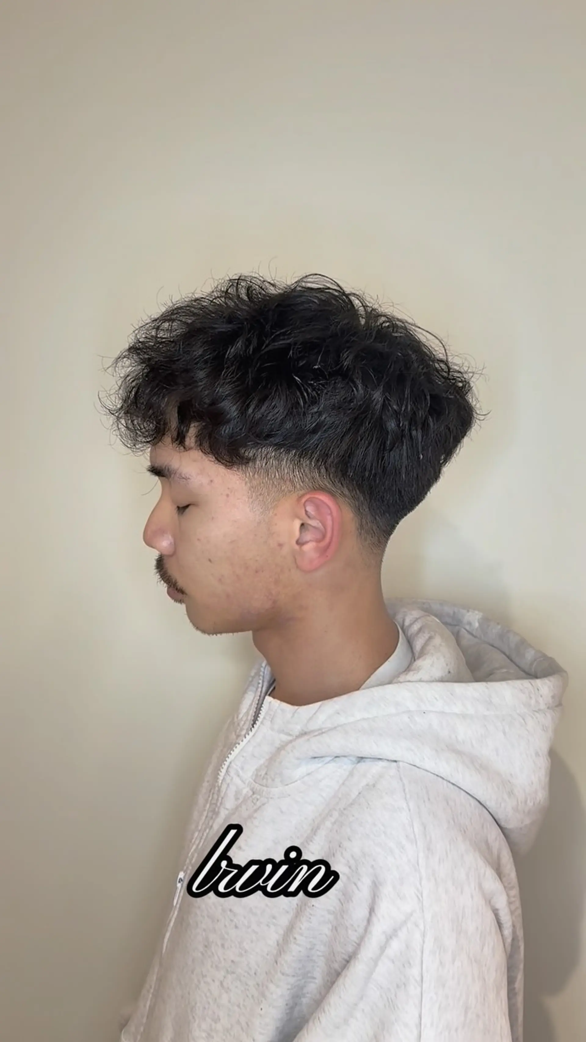 A textured curly crop haircut featuring full, voluminous permed curls on top paired with a clean low taper fade around the ear and nape. 1