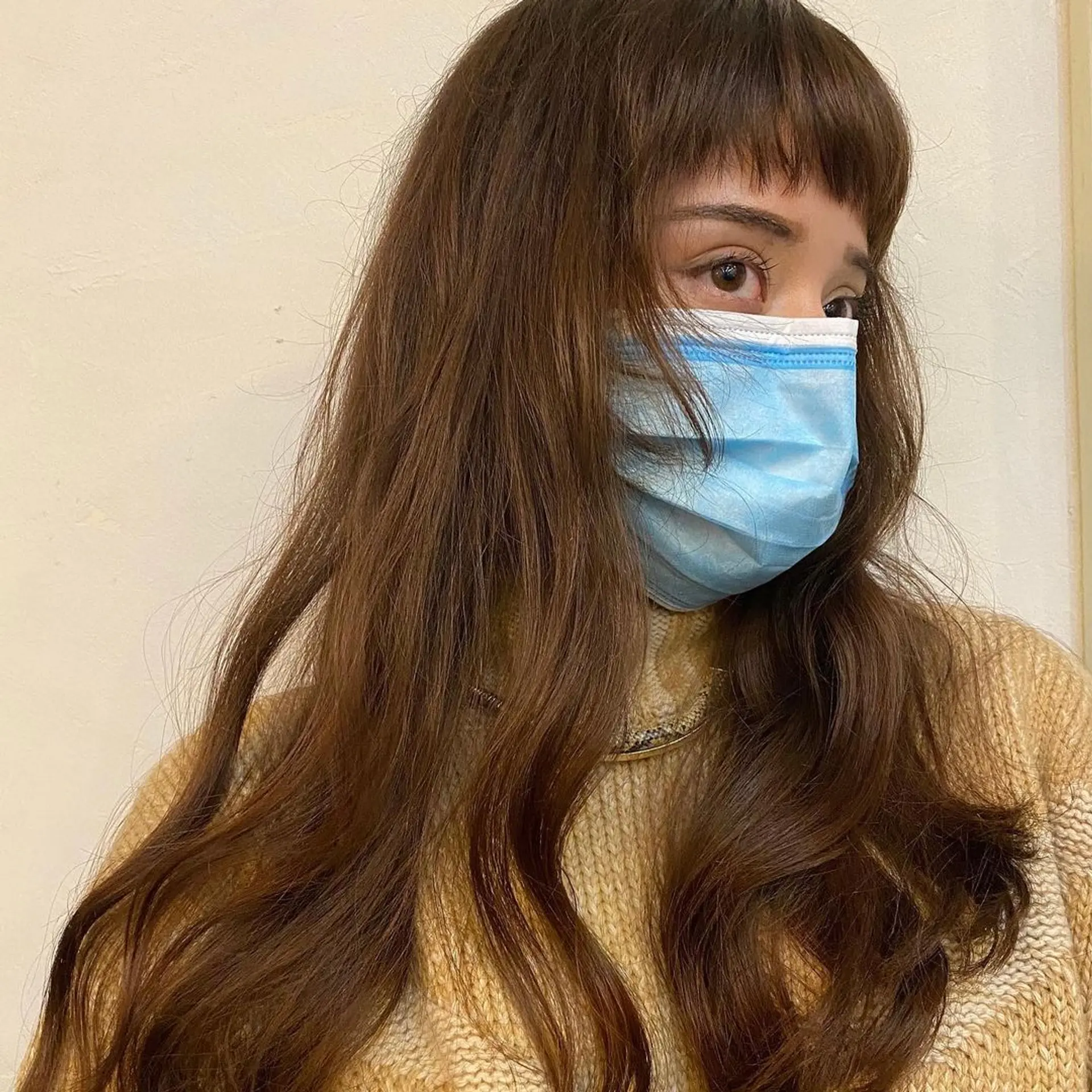 Long chestnut brown wavy hair with micro bangs. The hairstyle features natural, loose waves and layers that add dimension and movement by Coco. 1