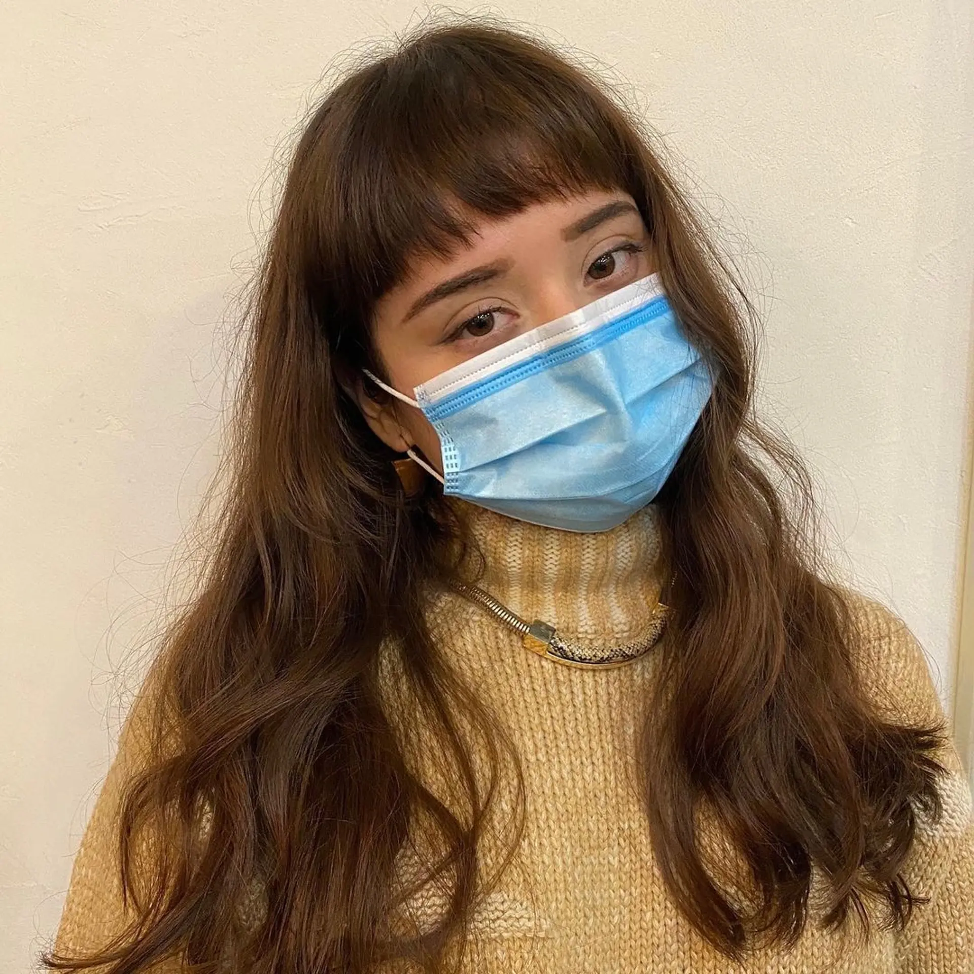 Long chestnut brown wavy hair with micro bangs. The hairstyle features natural, loose waves and layers that add dimension and movement by Coco. 3