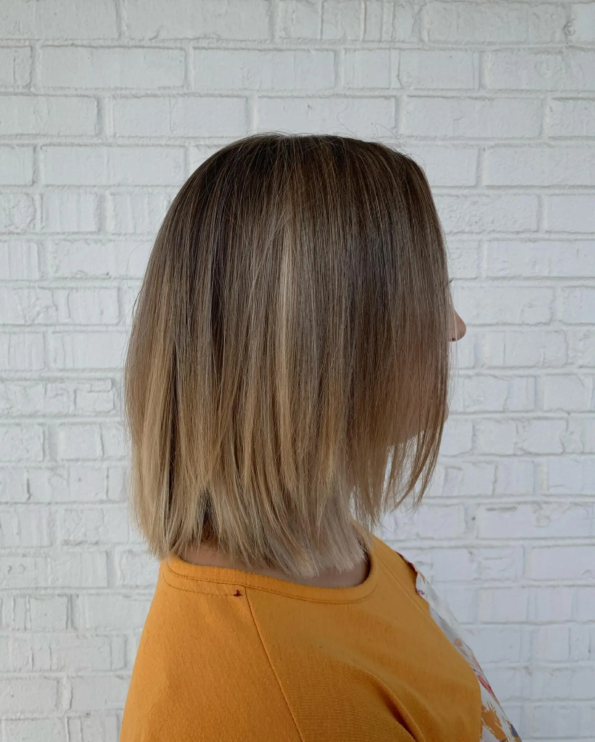 A straight, shoulder-length lob cut with a soft balayage blending natural light brown roots into warm honey-blonde tones. 1