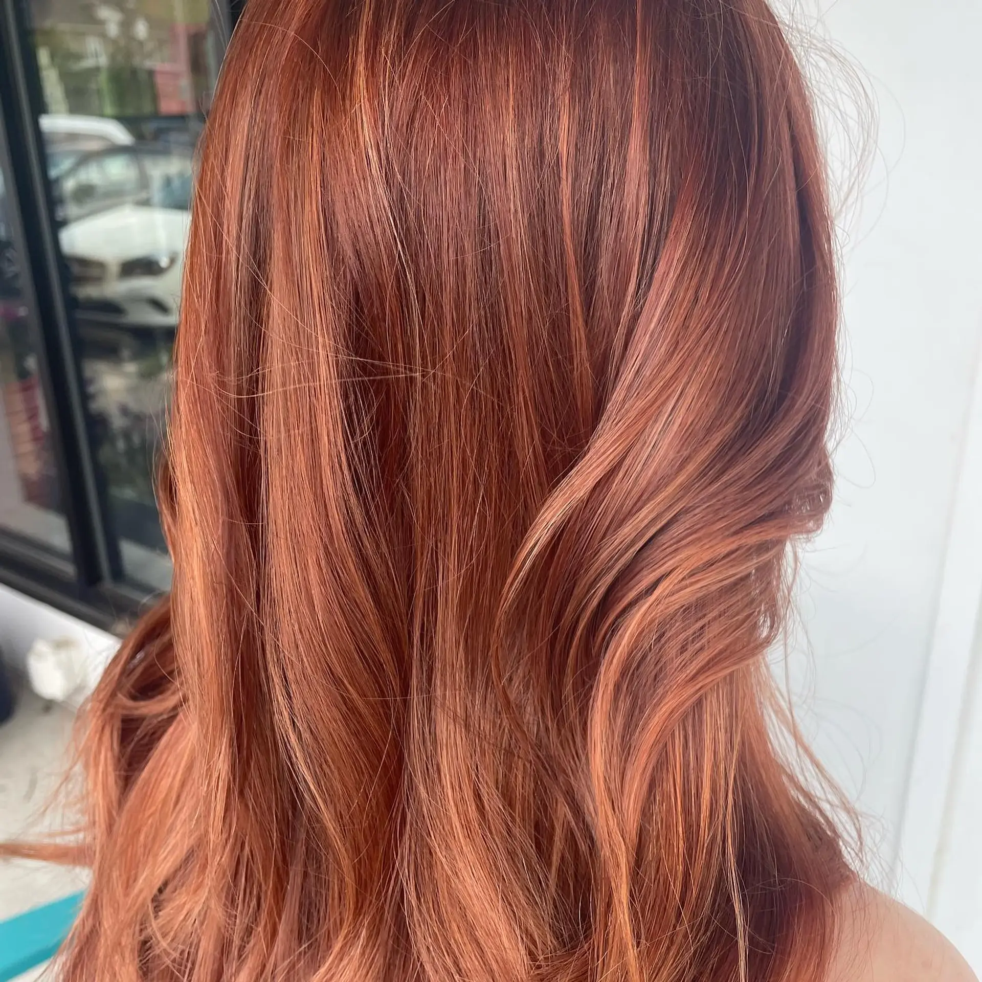 A vibrant peachy rose gold balayage styled with soft, loose body waves. 1