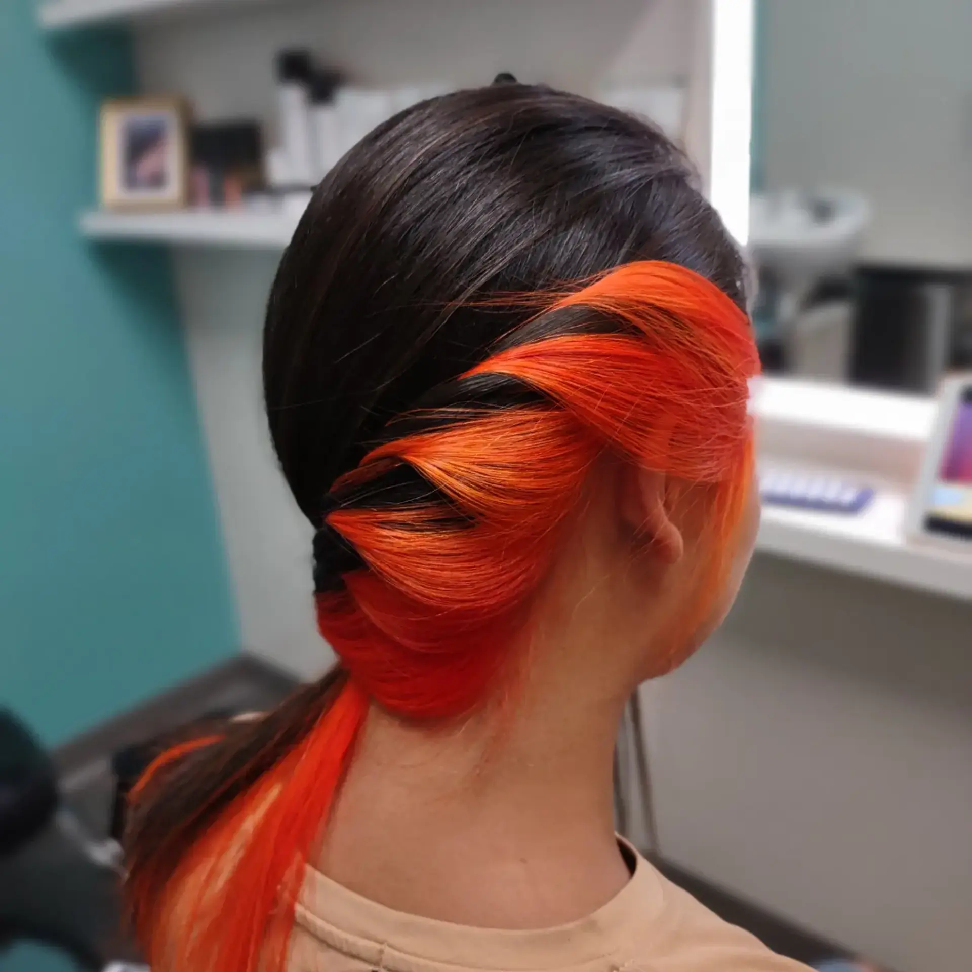 A sleek dark brown style twisted to the side to showcase striking neon orange peekaboo underlights. 1
