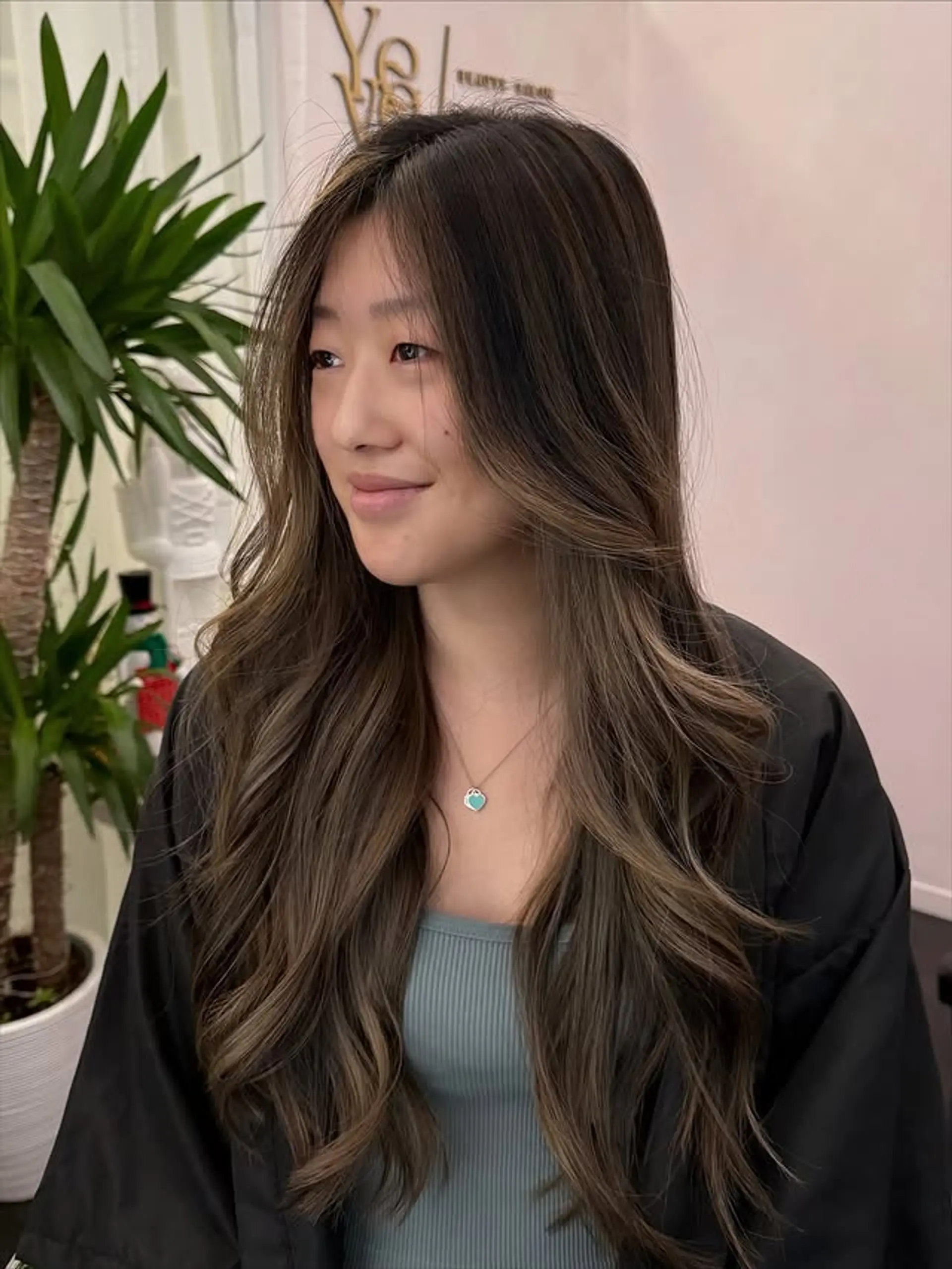 Long, wavy hair with subtle face-framing layers and natural balayage highlights in lighter brown and caramel tones, blending seamlessly with a dark brunette base. 1