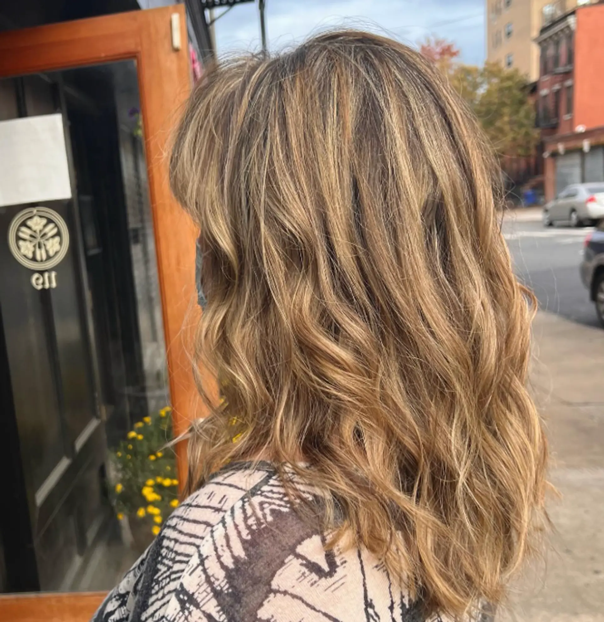 A medium-length wavy hairstyle with face-framing layers and a blended bronde color achieved through balayage. 1