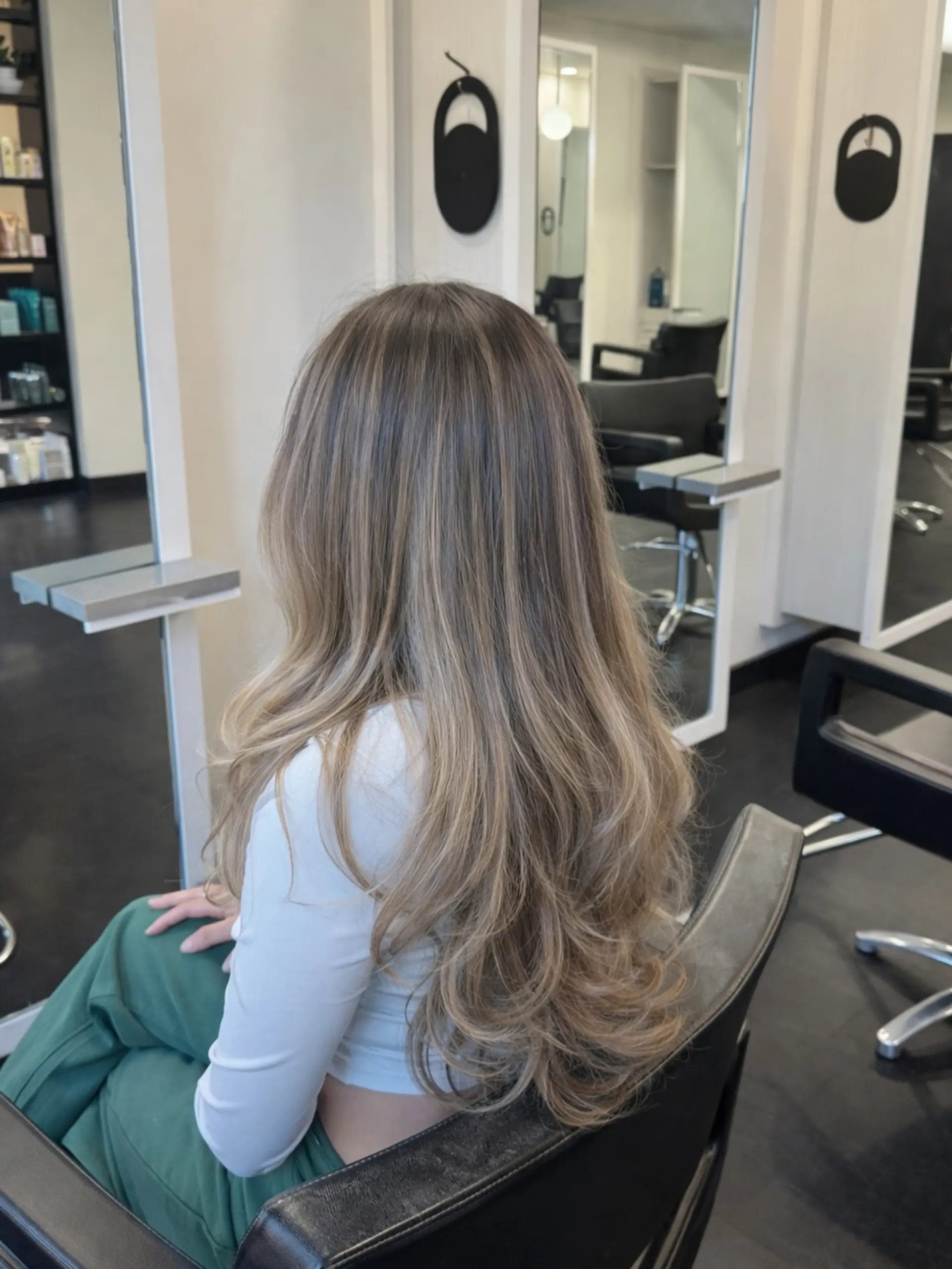 Long layered hair styled with soft, voluminous curls at the ends, showcasing a seamless dimensional blonde balayage with a shadowed root. 1