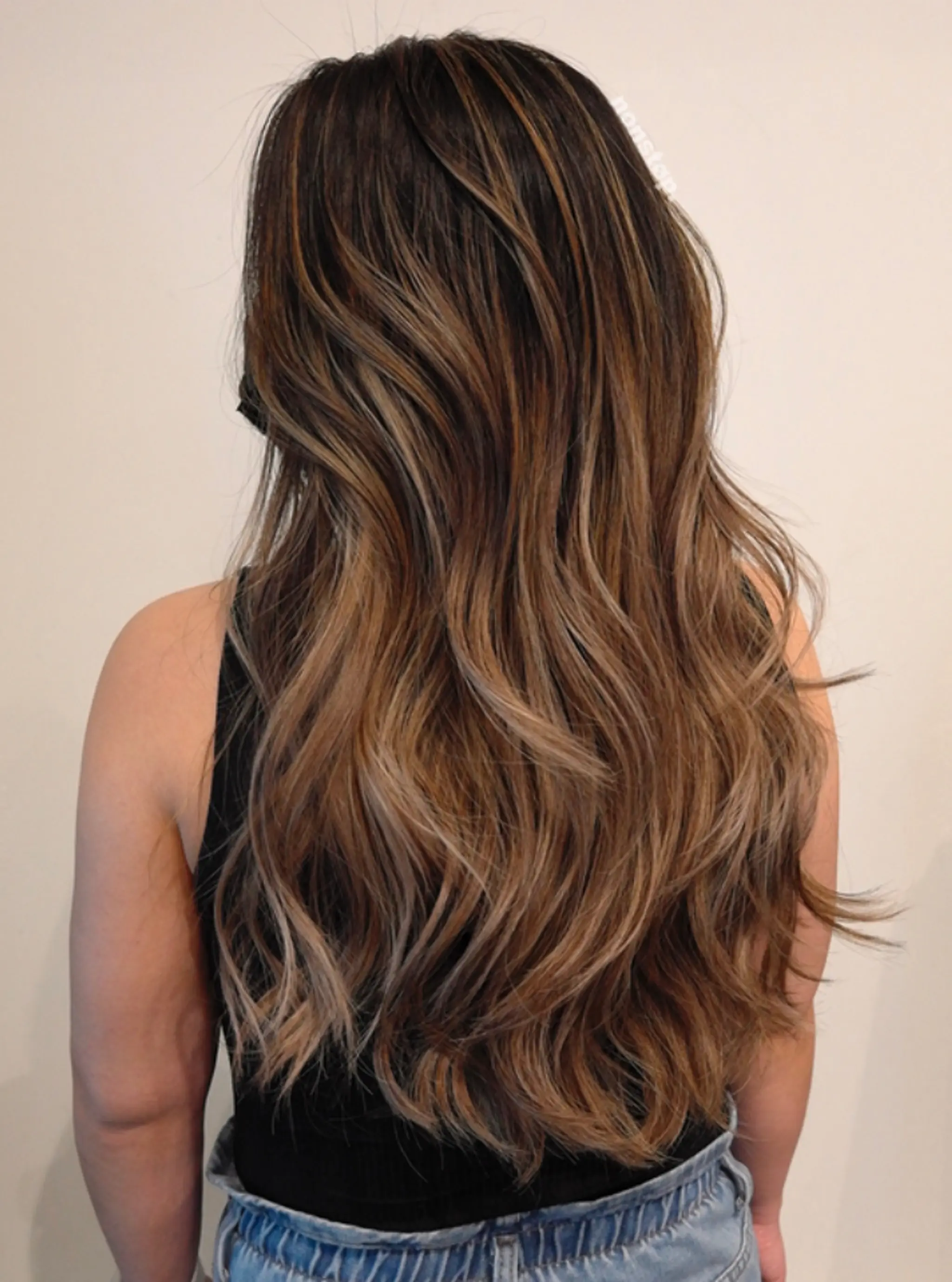 Long, wavy locks with a dark brown base transitioning into caramel and honey blonde highlights through balayage. Layered for added movement and dimension, enhancing natural waves. 1