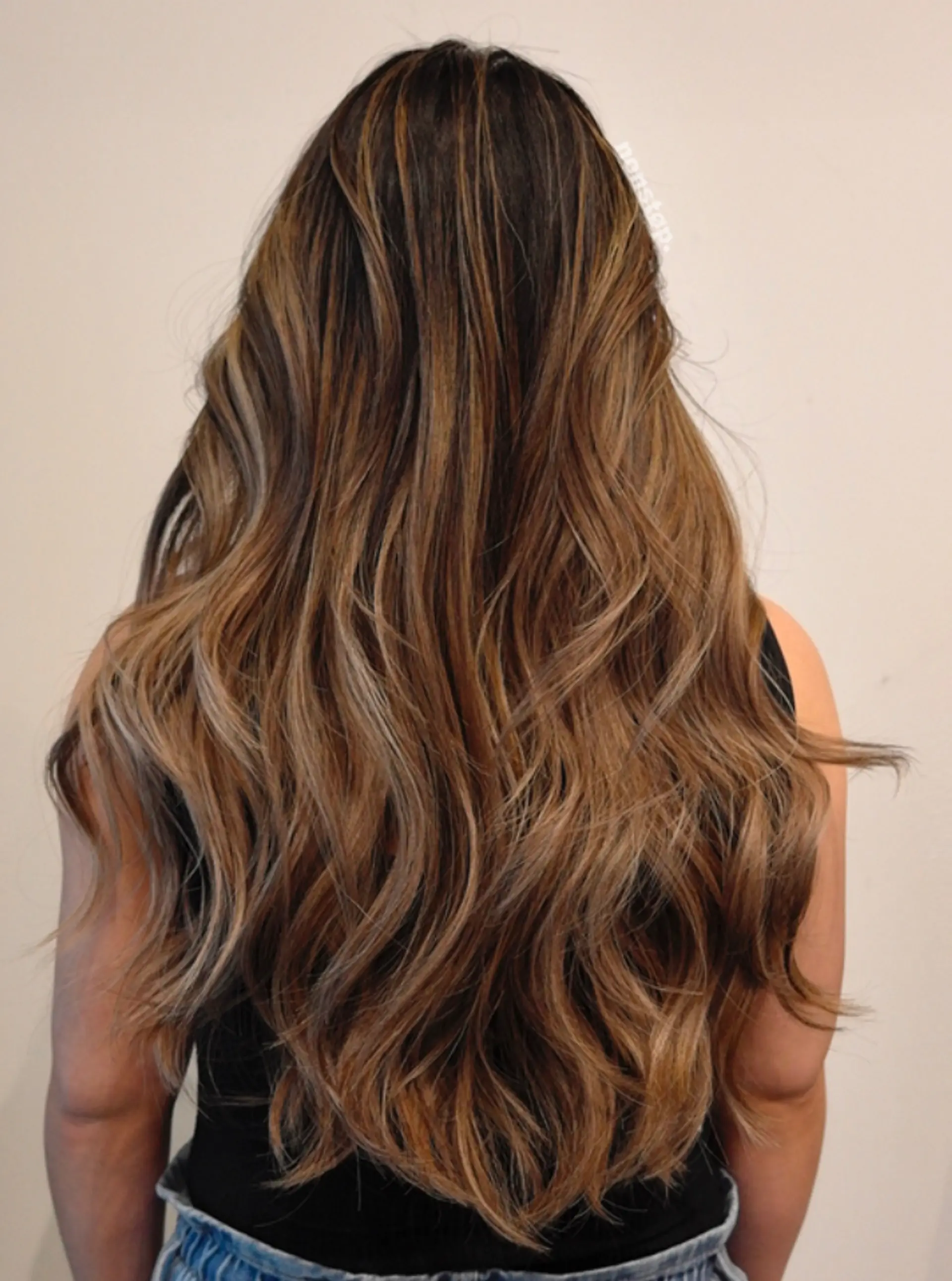 Long, wavy locks with a dark brown base transitioning into caramel and honey blonde highlights through balayage. Layered for added movement and dimension, enhancing natural waves. 2