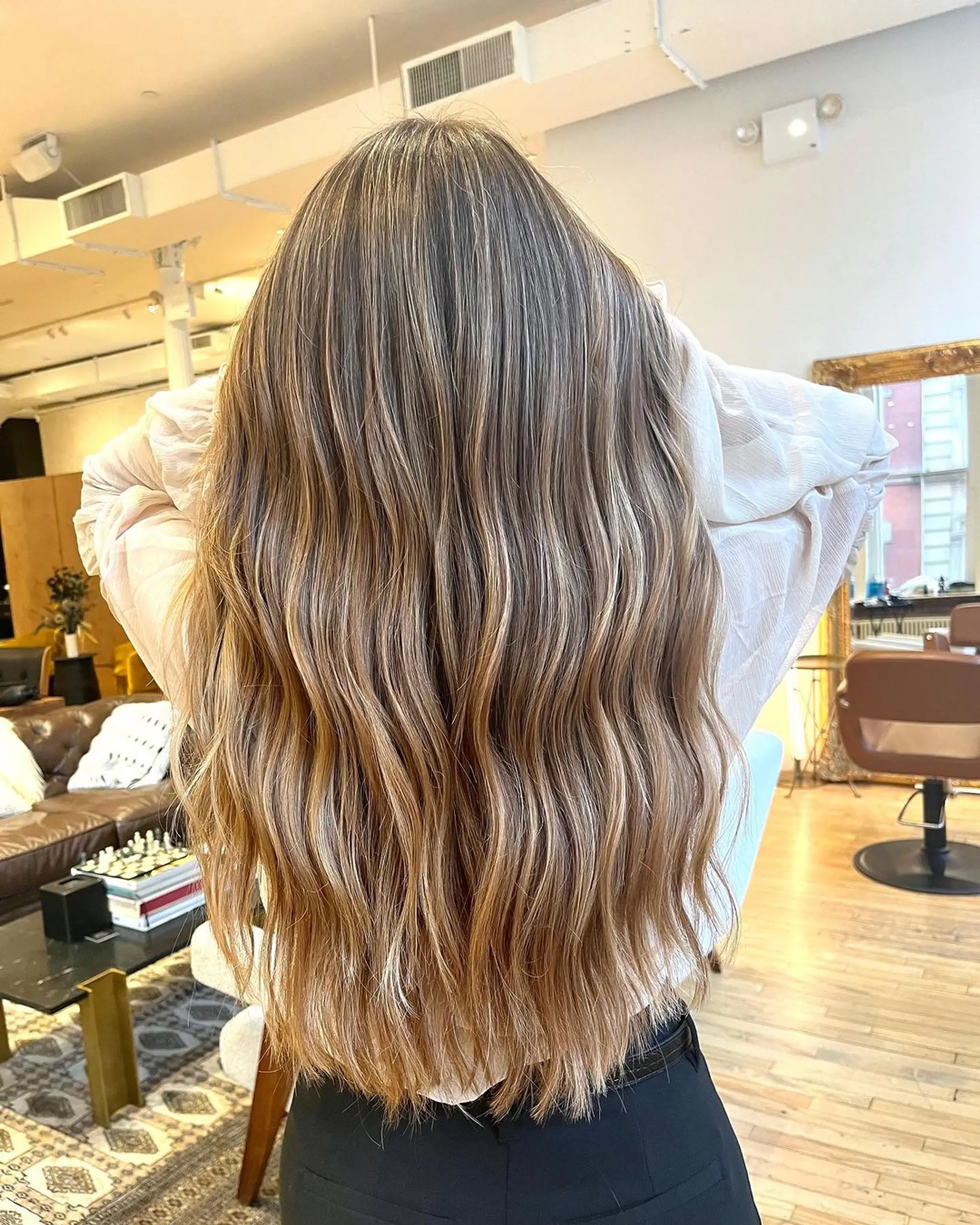 Long, wavy hairstyle with natural beach waves and a blend of blonde, light brown, and caramel highlights.