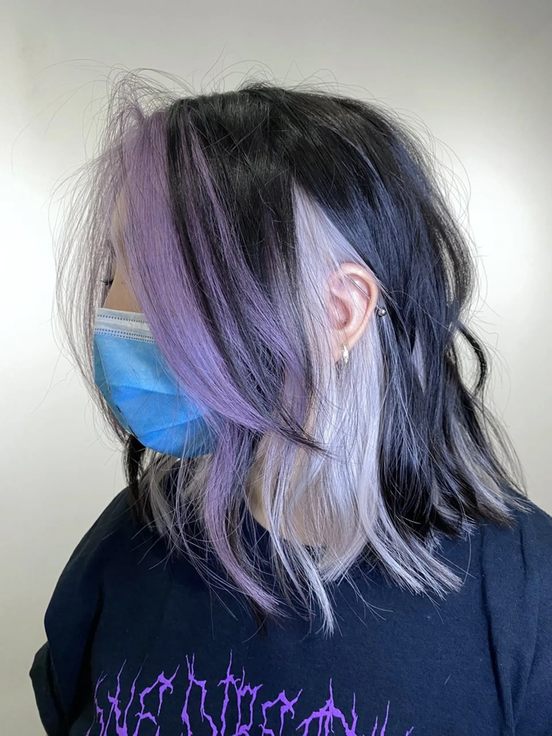 Medium-length wavy hairstyle with a black base, blending into lilac and silver tones. Features include face-framing highlights and layered choppy ends. 3