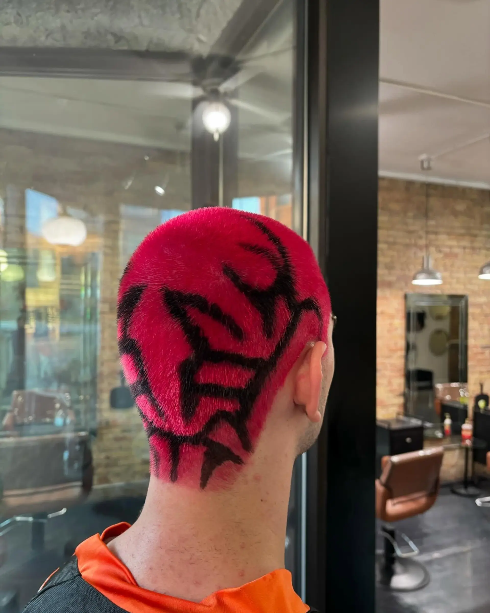 A vibrant hot pink buzz cut detailed with a bold, hand-painted black tribal graphic design across the back of the head. 1