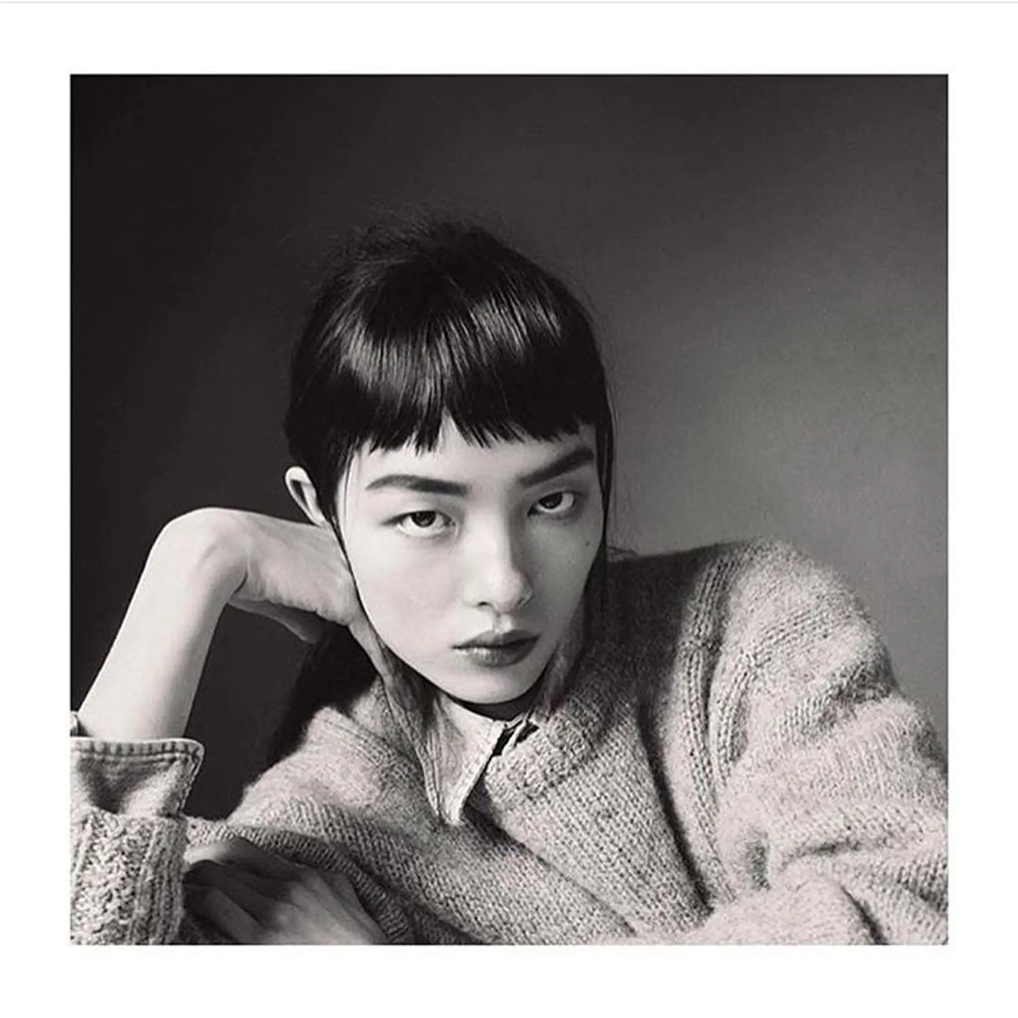 The hairstyle features sleek, medium-length black hair with short, blunt bangs, creating a modern and edgy look.