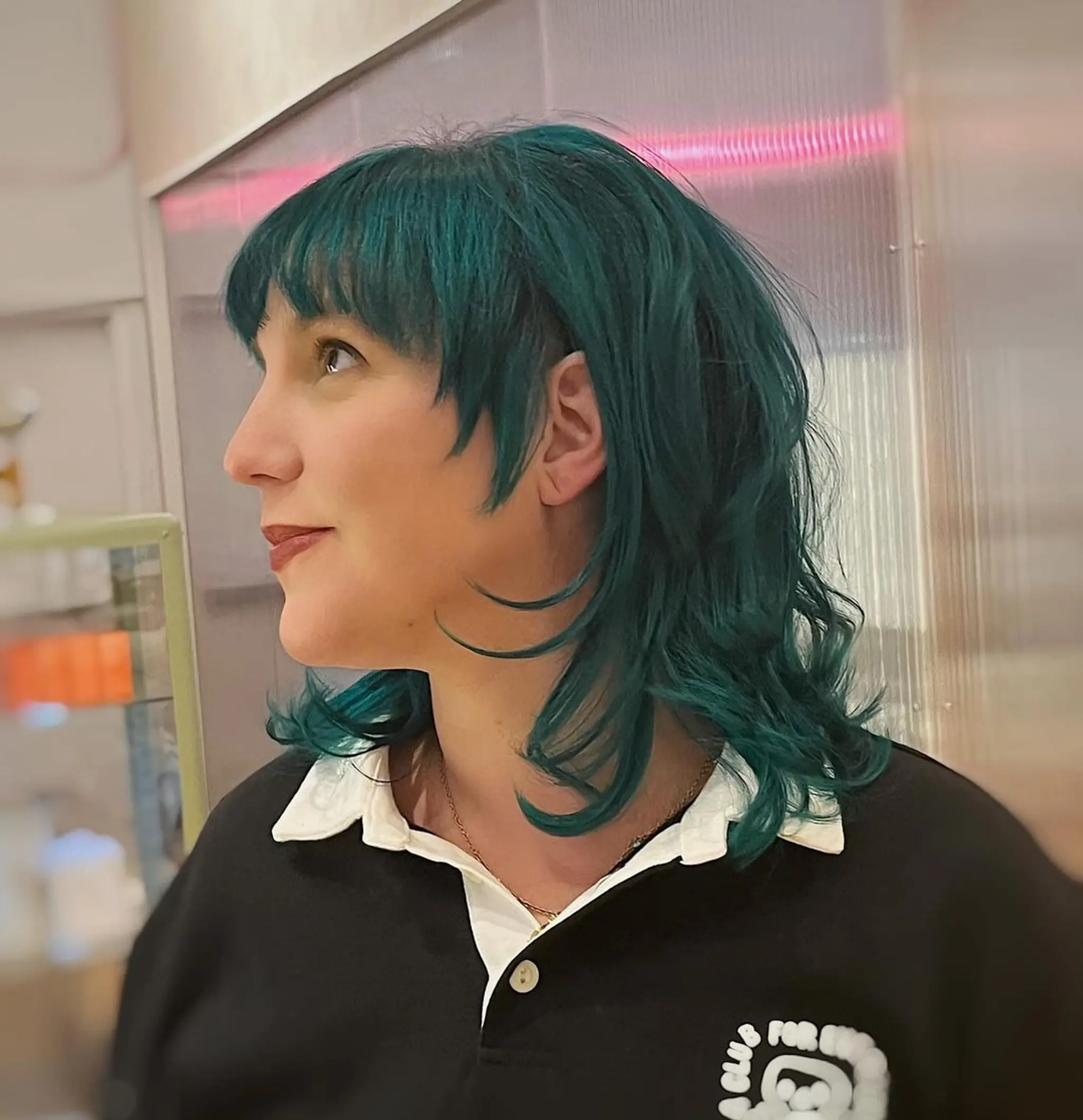 Emerald green wavy hair with fringe bangs, medium length, layered cuts, and feathered ends.