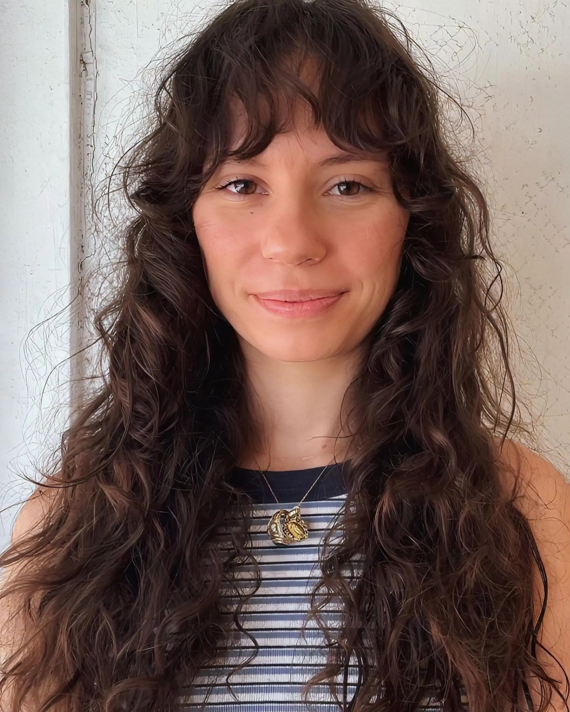 Long, dark brown wavy hair with natural waves cascading down and wispy bangs adding a playful touch. 1