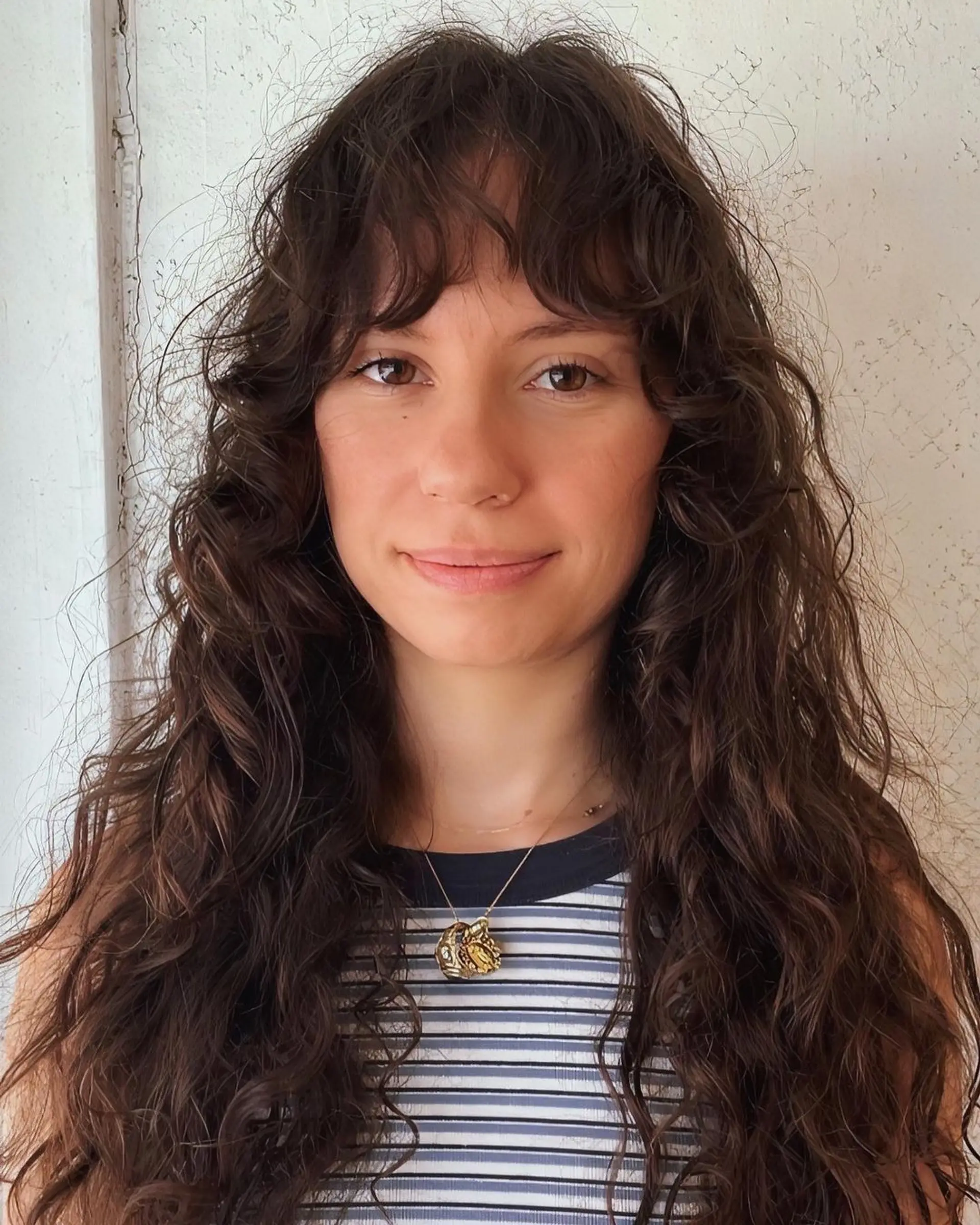 Long, dark brown wavy hair with natural waves cascading down and wispy bangs adding a playful touch. 2
