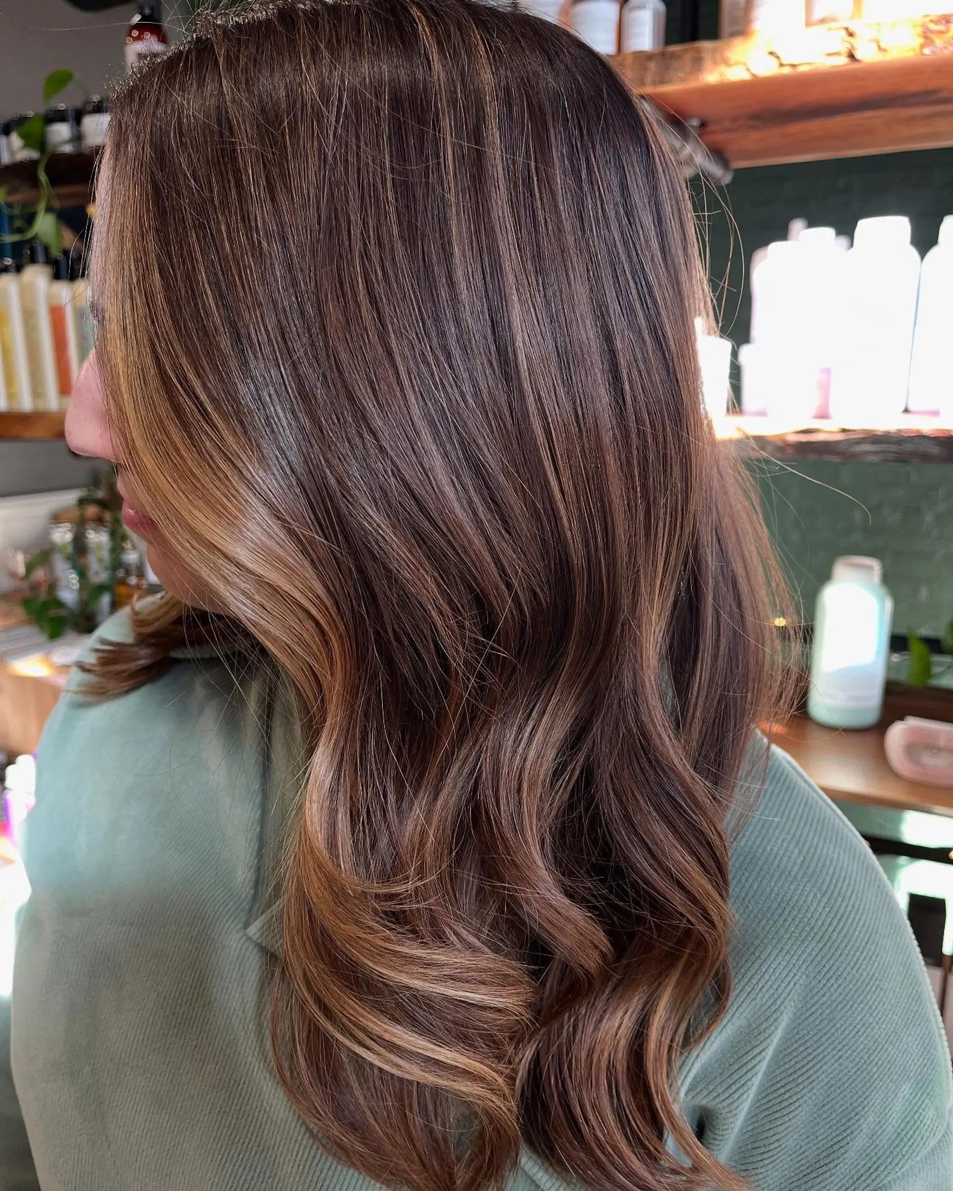 Rich brunette hair styled in glossy, loose waves with warm caramel dimensional highlights and a bright face-framing accent. 1