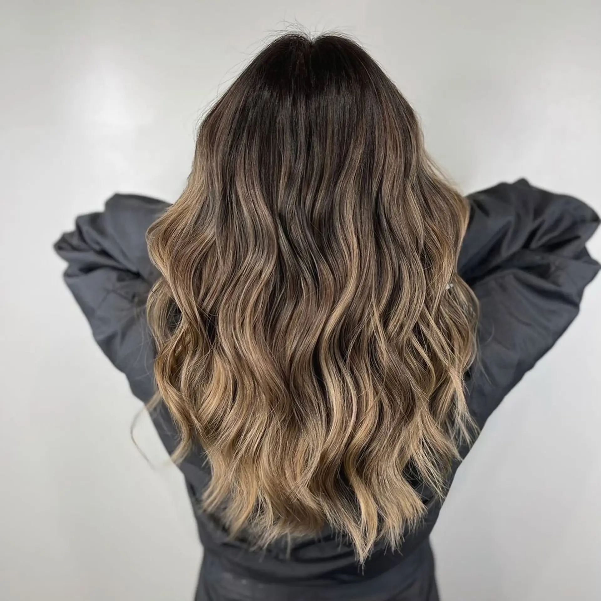 Dark brown roots transitioning into golden blonde ombre on long, naturally wavy hair with subtle layers.
Stylist - @xcellent_jason 1