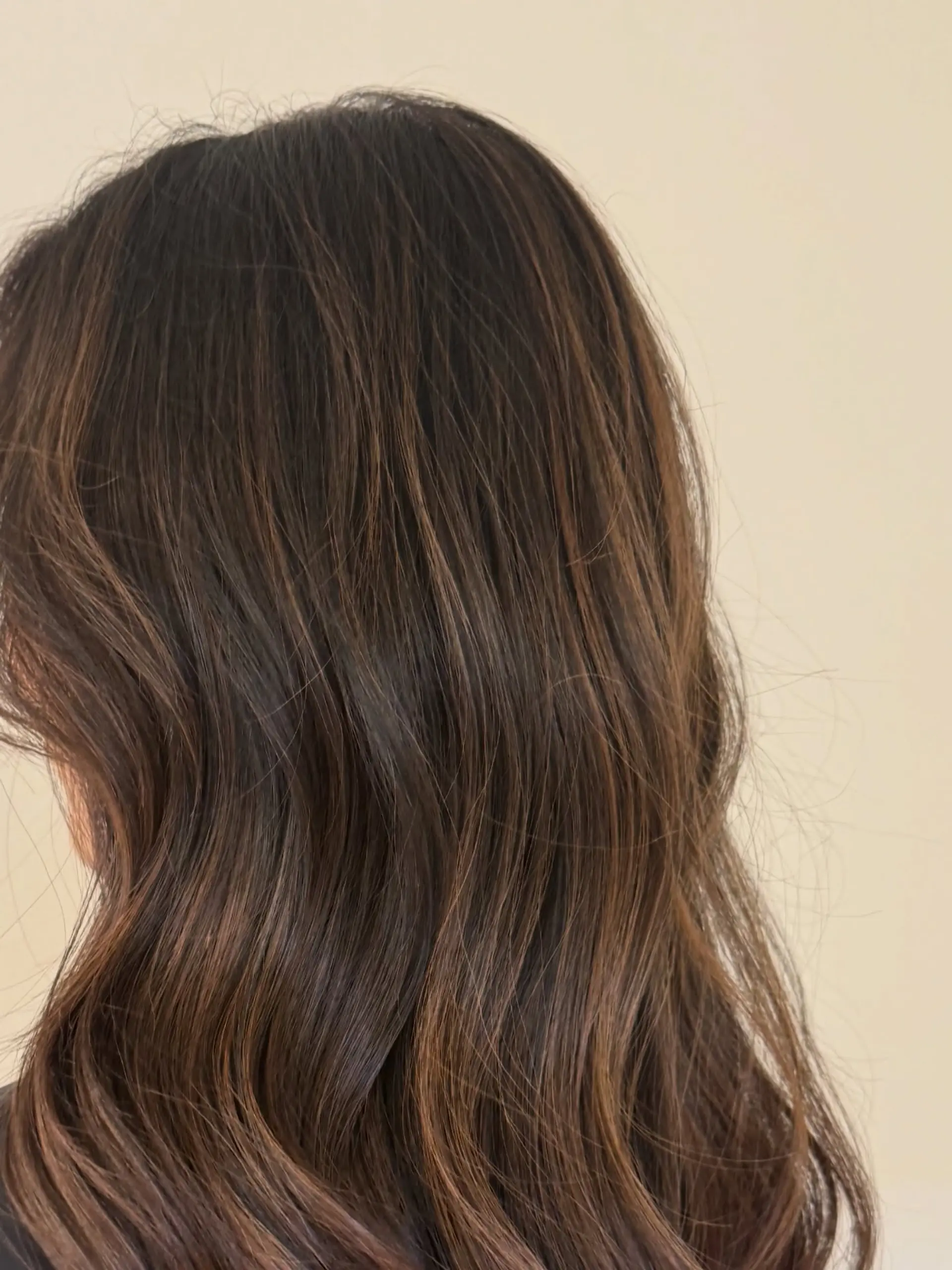 Medium-length dark brown hair featuring subtle warm balayage highlights styled in soft, effortless waves. 1