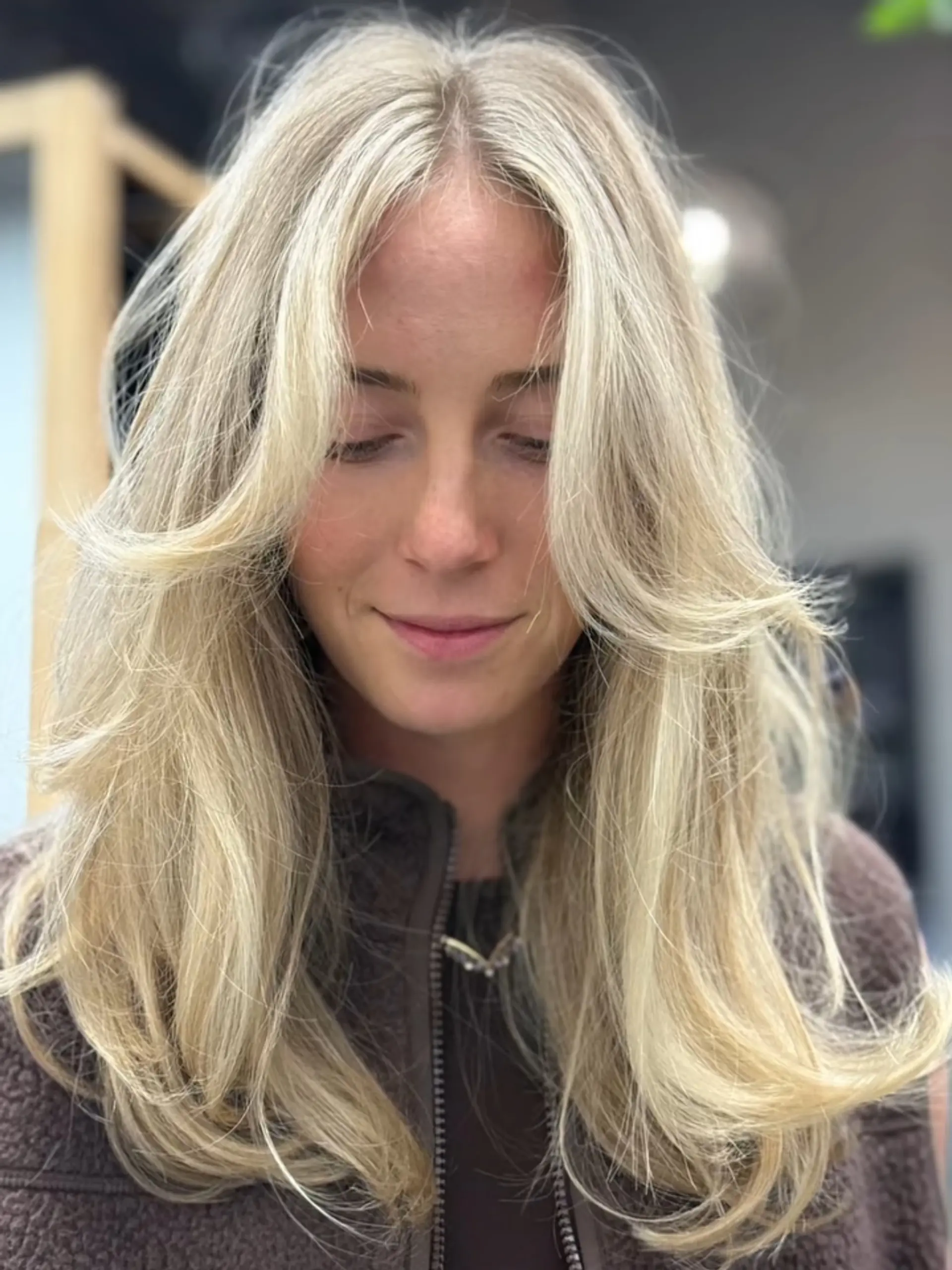 Long bright blonde hair styled with soft curtain bangs and layered, outward-swept ends. 1