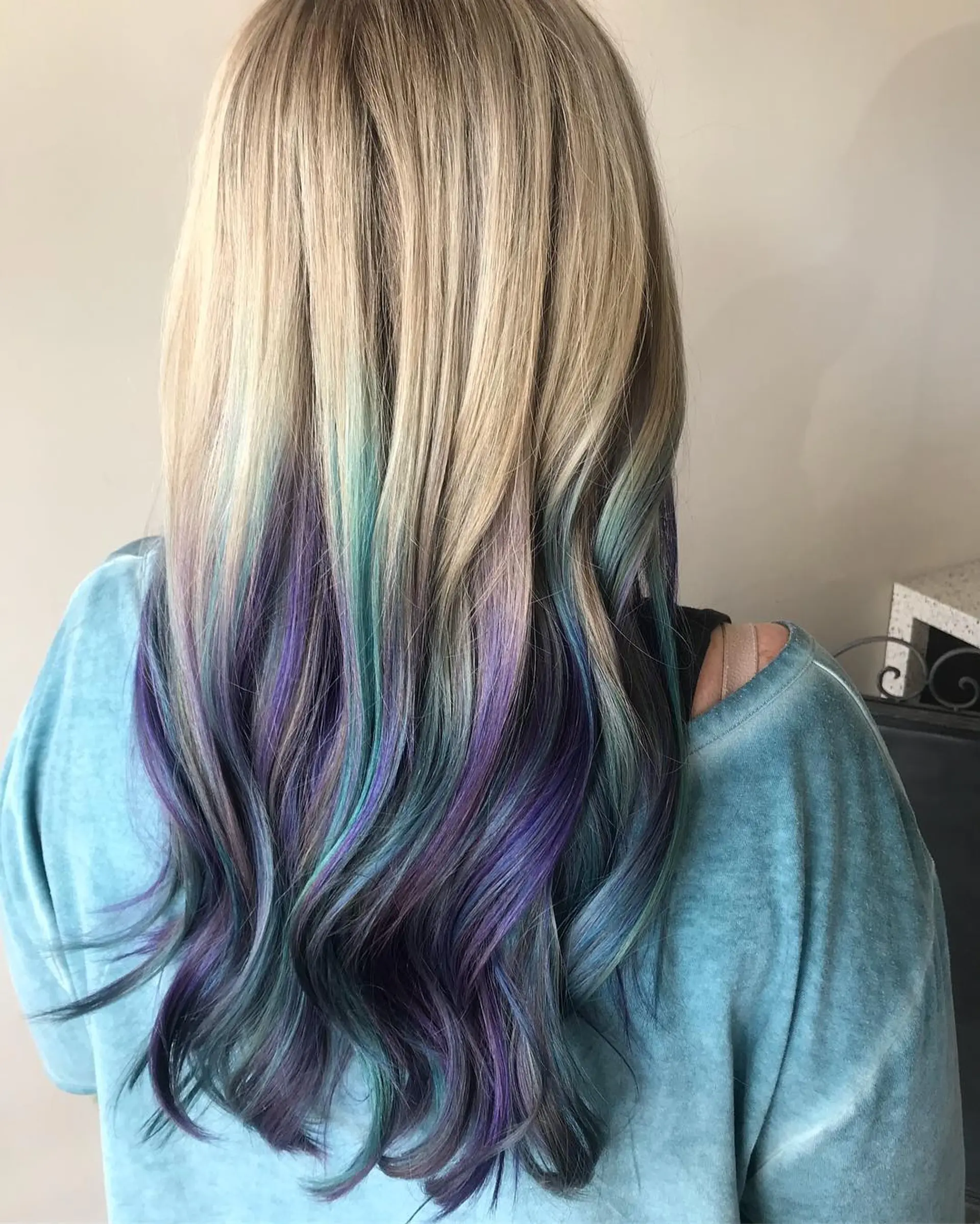 Long ash blonde hair styled in loose waves, revealing a vivid peekaboo underlayer of purple, teal, and blue shades. 1