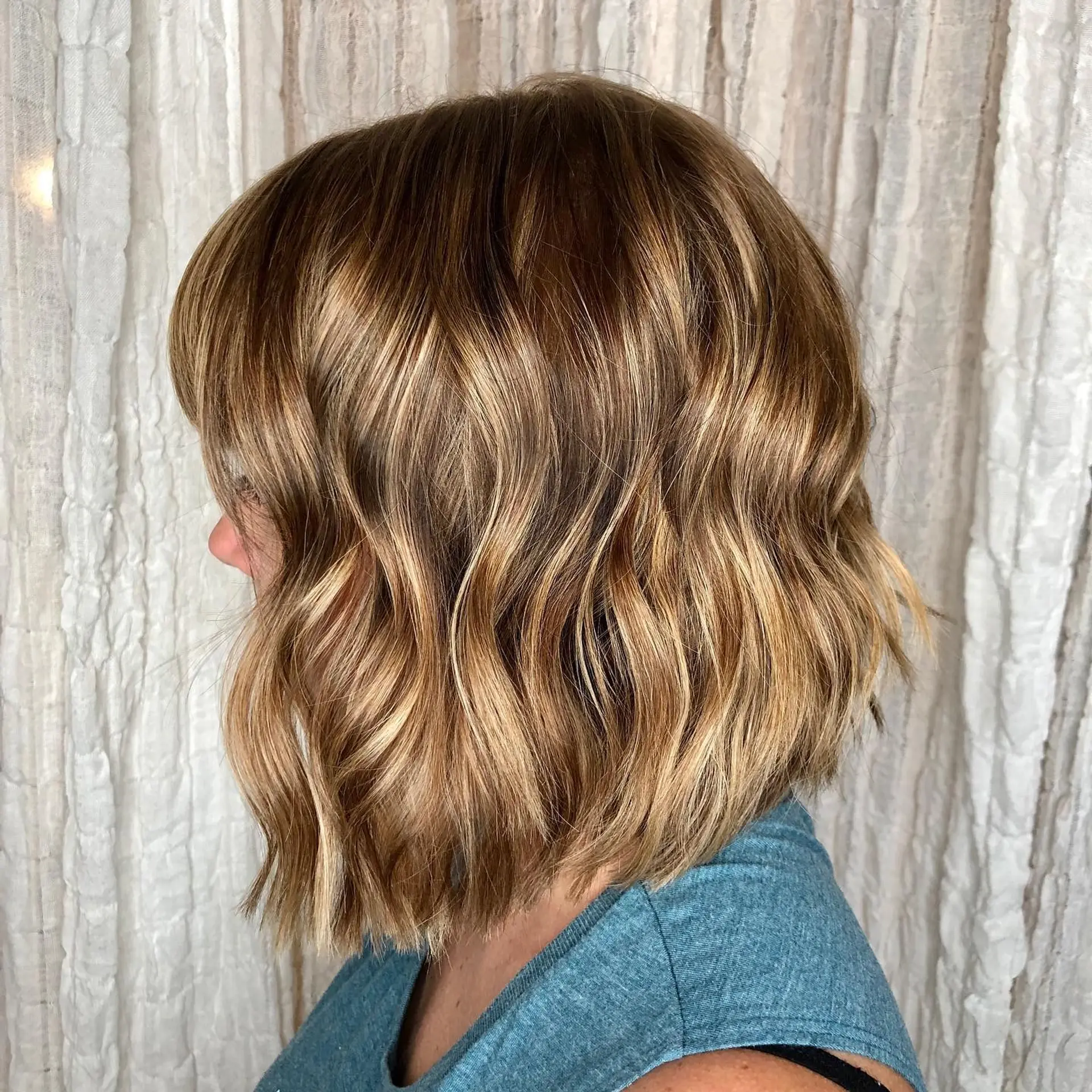A textured wavy bob featuring warm golden babylights blended over a light brown base with soft bangs. 1