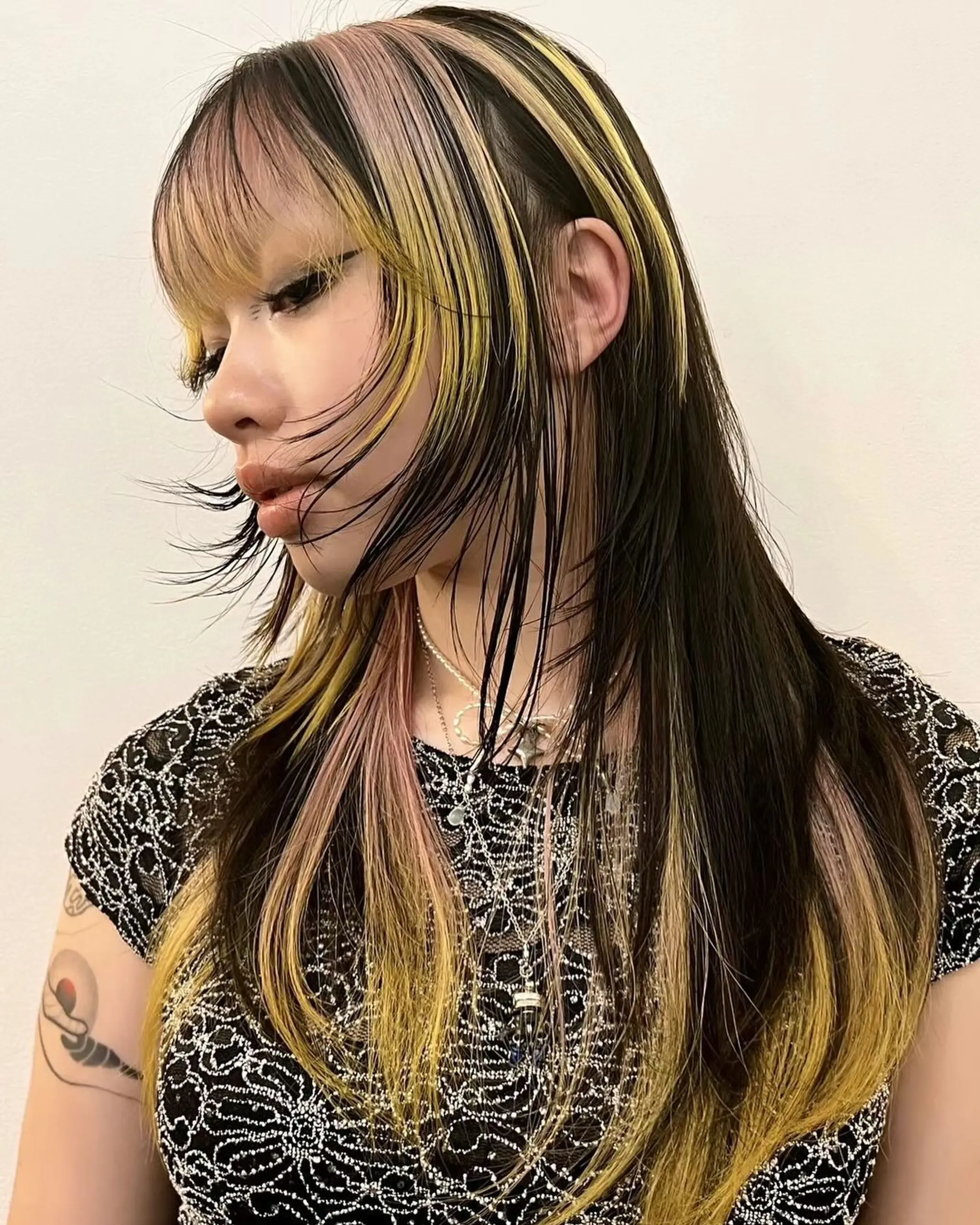Long hairstyle with multi-tone color blending, featuring long feathered layers and blunt bangs with contrasting highlights.