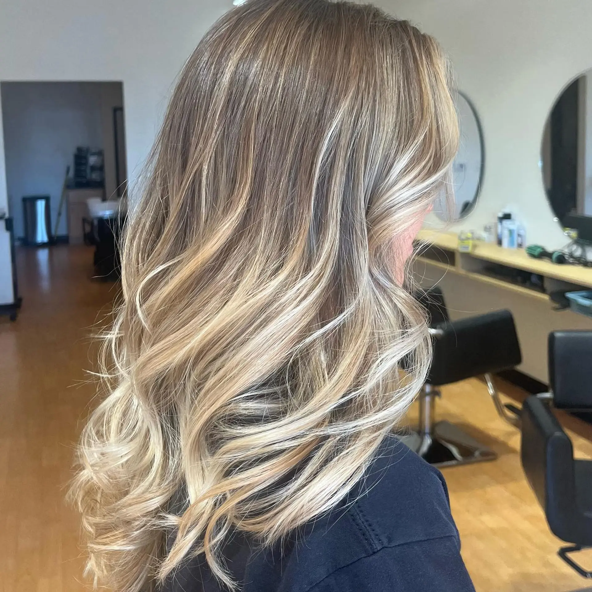 Long, dimensional blonde balayage styled into loose, flowing waves with soft face-framing highlights. 1
