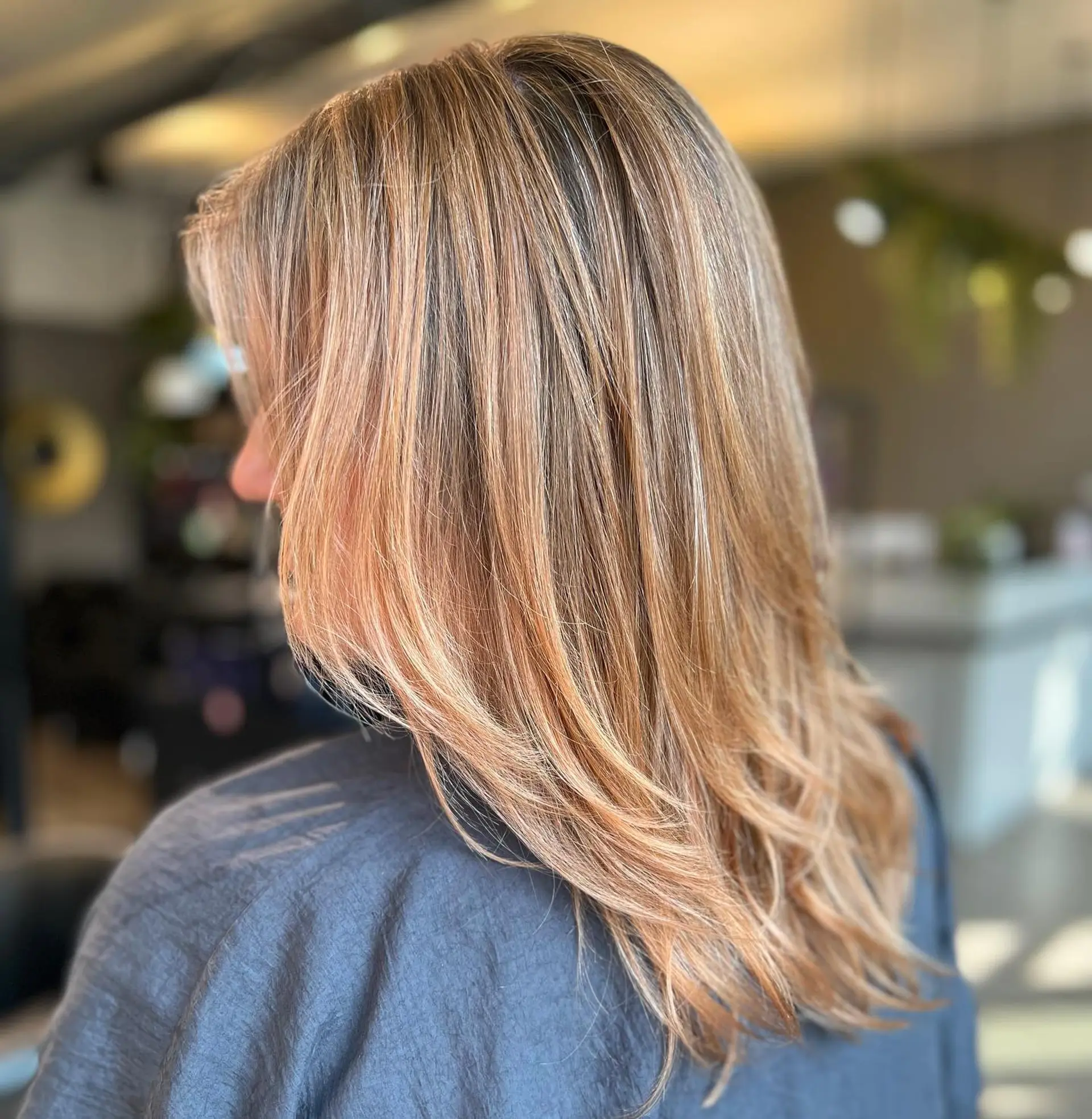 A medium-length hairstyle with subtle layers and a blended strawberry blonde balayage. 1